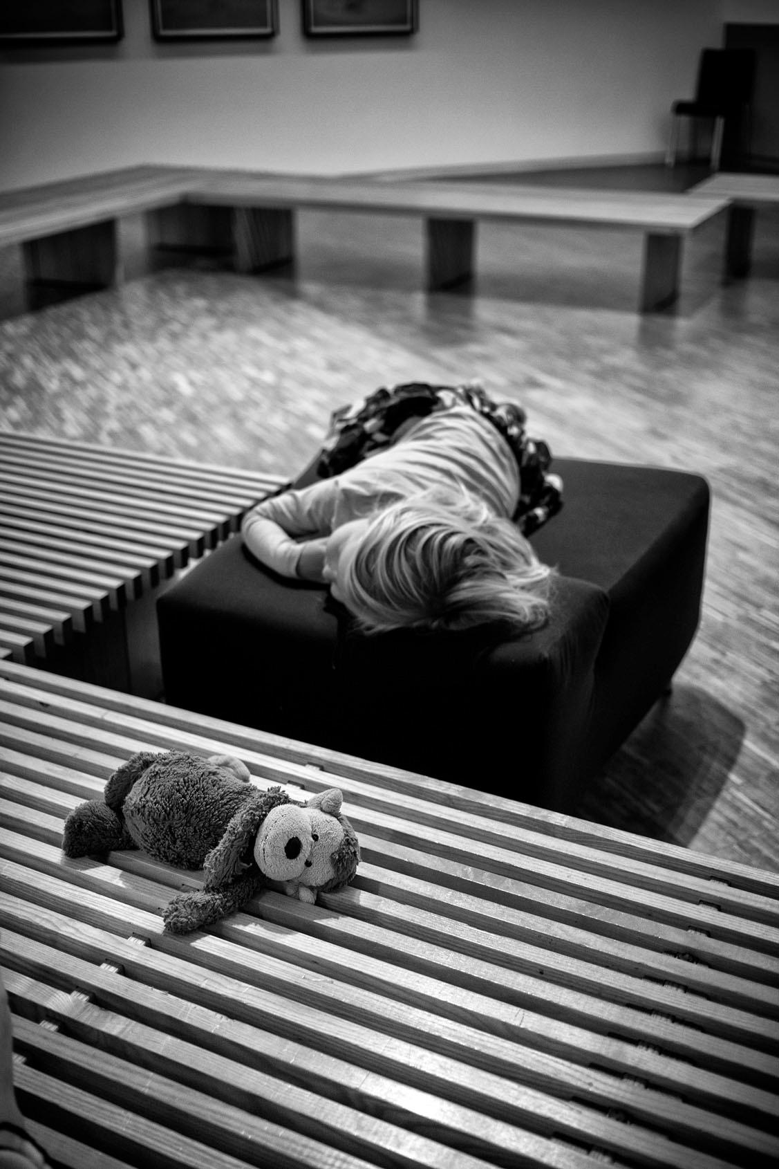 Black and White Photograph Gérard Uféras - Un jour au musée - enfant allongé sur le canapé avec un ours en peluche