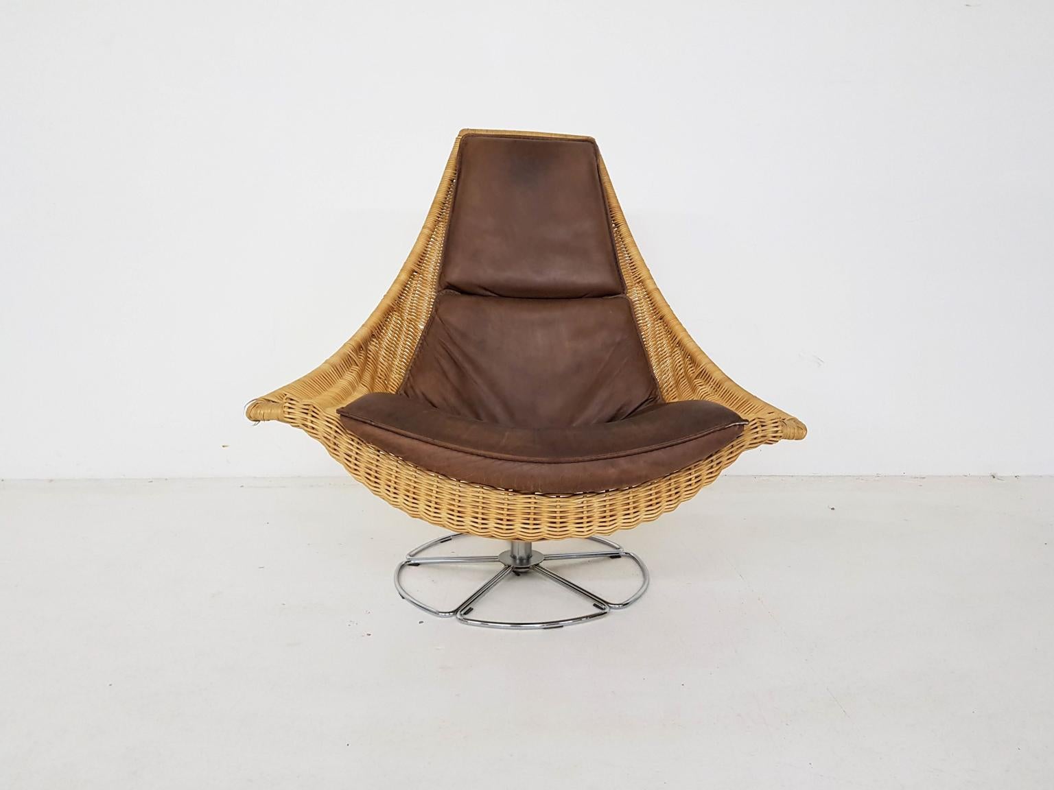 A comfortable lounge chair made of wicker with leather cushions on a metal round foot. This chair is designed by the Dutch Gerard Van Den Berg and part of his rattan or wicker series furniture. This is the more rare edition with the metal foot.