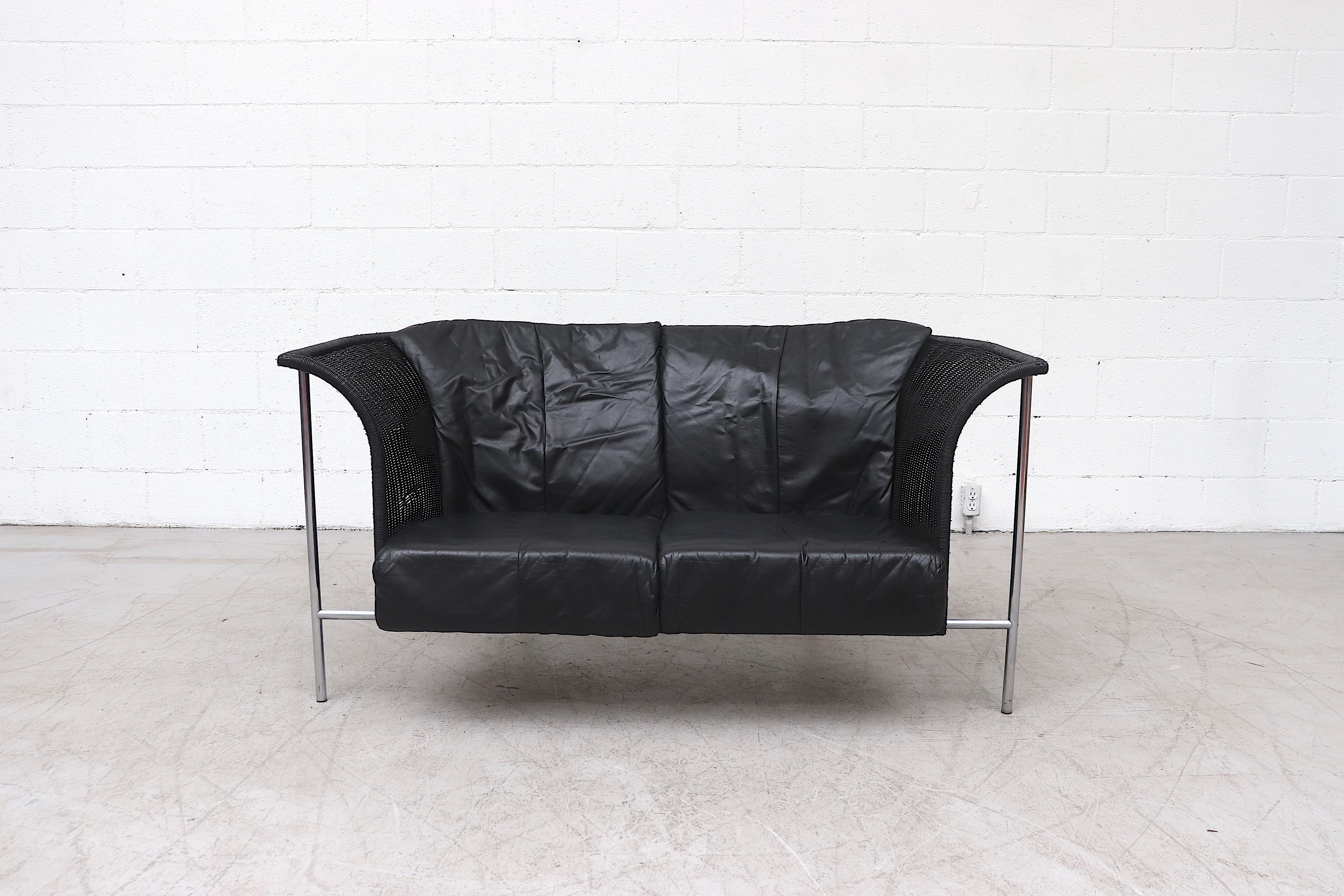Handsome Gerard van den Berg style wing back black rattan 2-seat sofa with black leather cushions on tubular chrome frame. In original condition with light rattan breakage and some light frame rust.