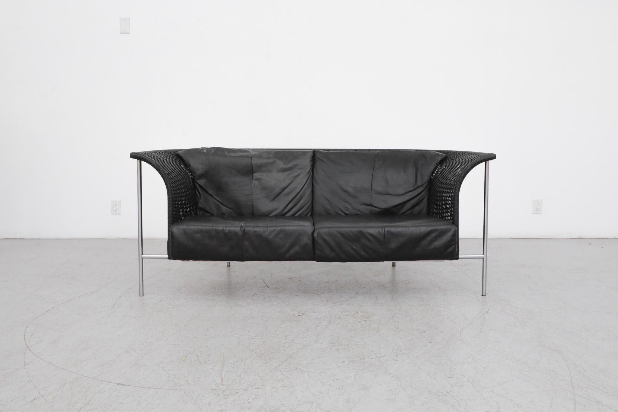 Gorgeous Gerard van den Berg wing back loveseat for Rohe Noordwolde in black rattan with black leather cushions. This seemingly floating loveseat sits on a tubular chrome frame and has new plywood seat supports that have replaced the original rubber