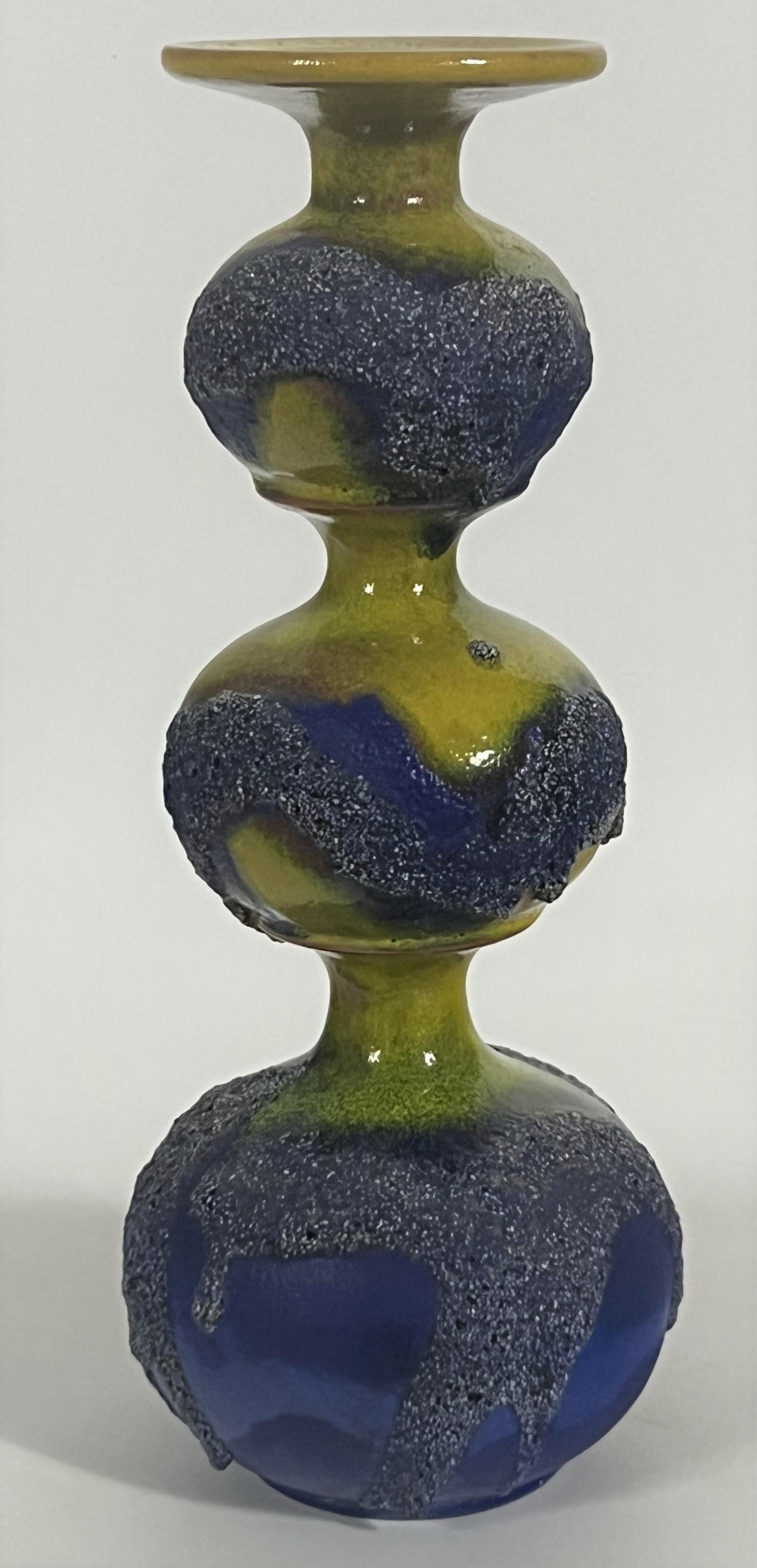 Gerda Heuckeroth at Carstens Tönnieshof. Gerda is among a handful of designers whose work in German Fat Lava ceramic design was credited by name then and now. This tall candle holder features an exciting crusty blue volcanic glaze over an yellow