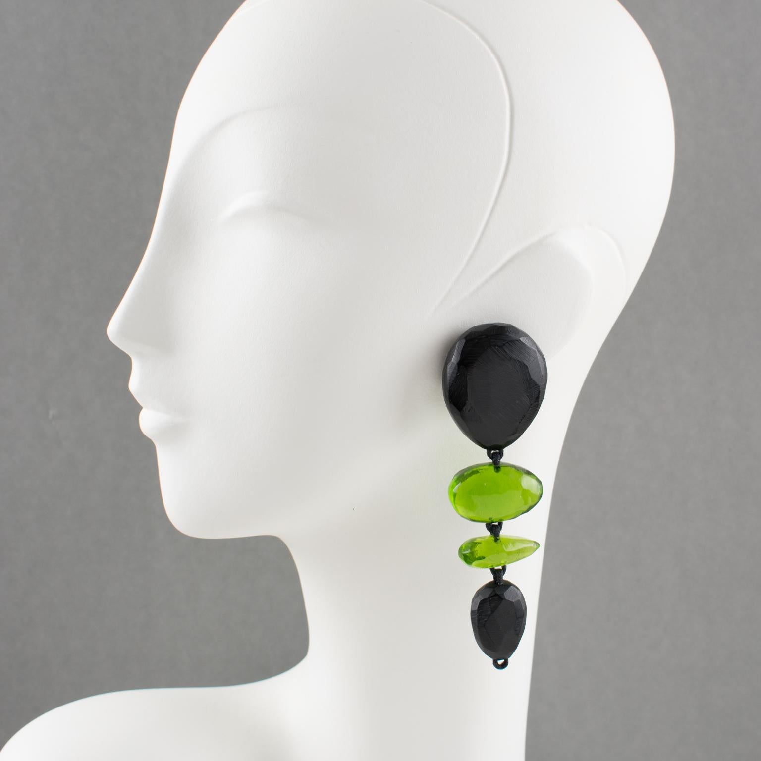 Charming oversized clip-on earrings by Gerda Lyngaard for Monies. Dangling pebble and drop shape in Lucite or resin with a textured pattern. Assorted colors of ebony black and transparent olive green. Marked 'Monies' on the clasp. 
Measurements: