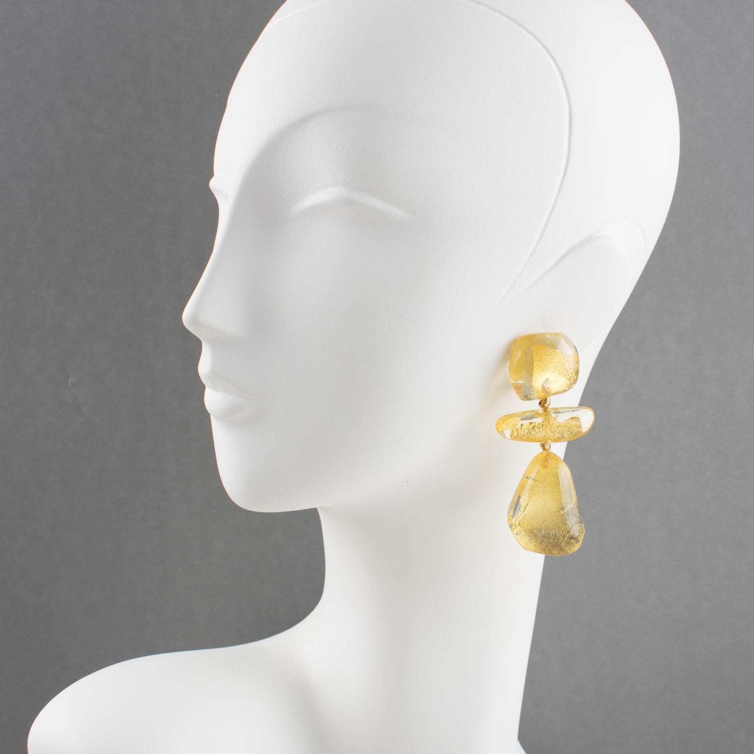 Stunning oversized clip on earrings by Gerda Lyngaard for Monies. Dangling pebble and drop shape with crystal clear Lucite or resin and gold foil inclusions. Marked 'Monies' on clasp. 
Measurements: 2.88 in. high (7.3 cm) x 1.38 in. wide (3.5 cm)