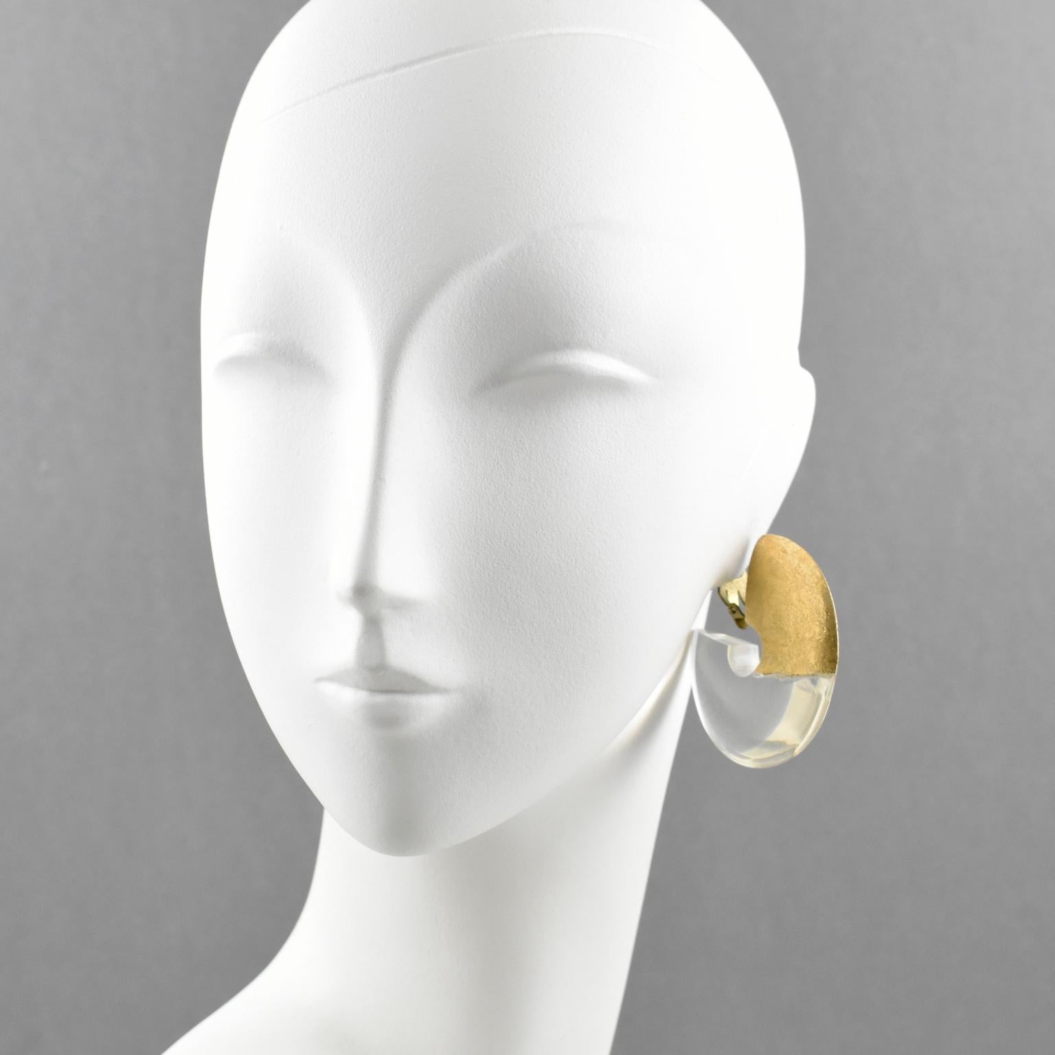 Stylish oversized hoop clip-on earrings by Gerda Lyngaard for Monies. Crystal clear acrylic or Lucite and gold foil application. Marked 'Monies' on the clasp. 
Measurements: 2.07 in. diameter (5.2 cm) x 0.38 in. thick (1 cm)