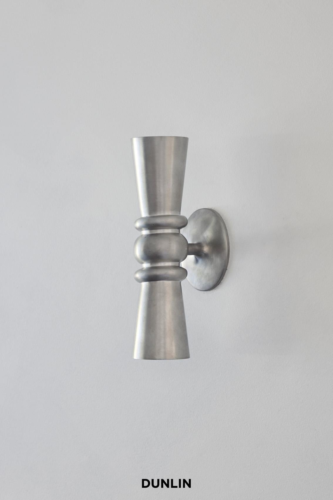 Handmade in solid brass exclusively for Dunlin. 

The Dunlin Germaine Weathered Brass Up-Down Wall Light exudes an elegant and charming presence, adding a touch of sophistication to any living room. Its meticulous craftsmanship, with a keen focus on