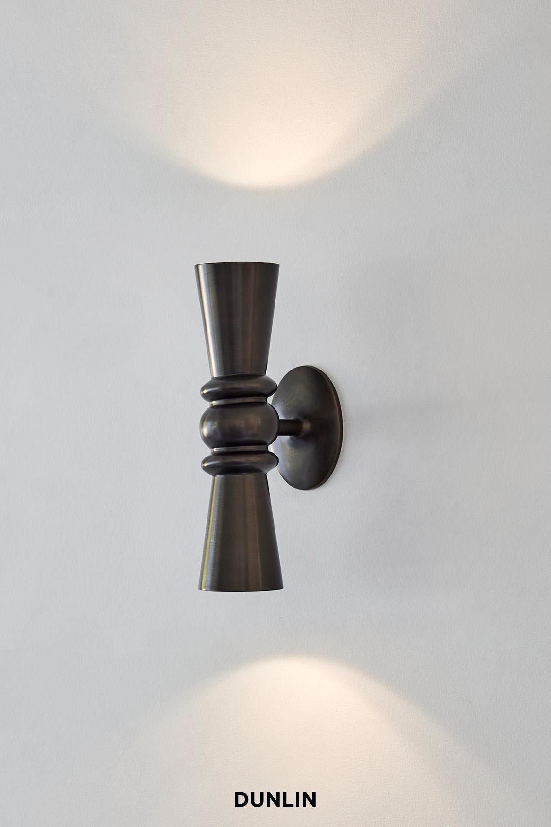 Handmade in solid brass exclusively for Dunlin. 

The Dunlin Germaine Weathered Brass Up-Down Wall Light exudes an elegant and charming presence, adding a touch of sophistication to any living room. Its meticulous craftsmanship, with a keen focus on