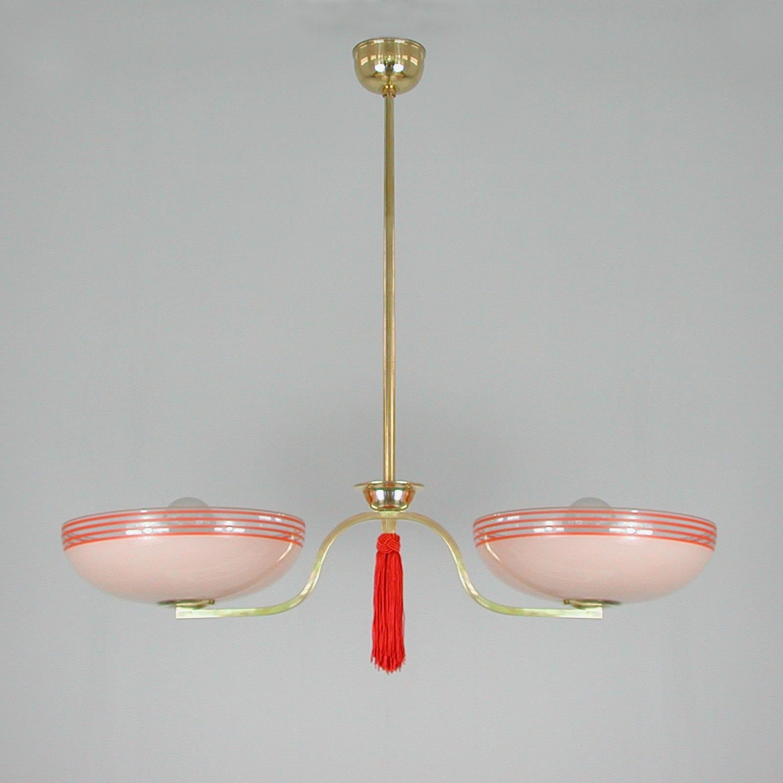 This unusual fixture was designed and manufactured in Germany in the 1930s during the Bauhaus period.
It features two pale pink and red glass lampshades, a ruby red tassel and brass hardware.

The light has been rewired and requires two E27