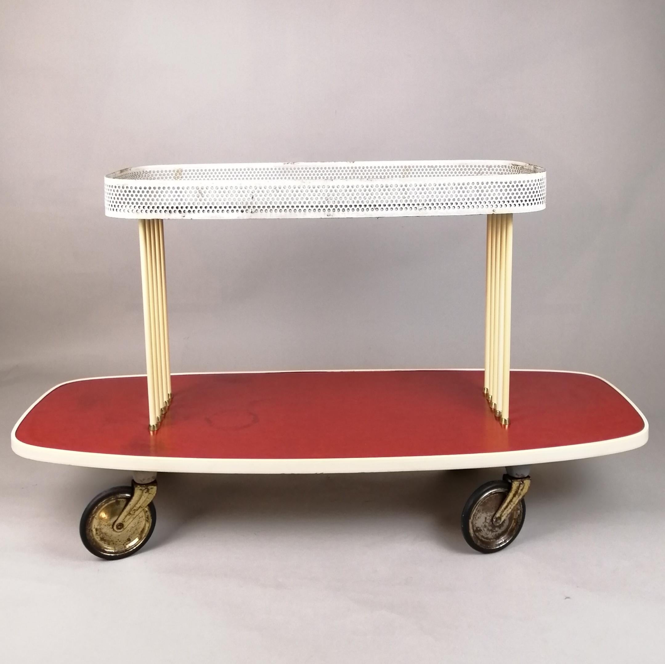 Carrello di servizio moderno della metà degli anni '60 nello stile di Mathieu Matégot. Le superfici ovali in formica grigia e rossa sono sostenute da un gruppo di 5 tubi laccati color crema con dettagli in ottone. La superficie superiore è dotata di