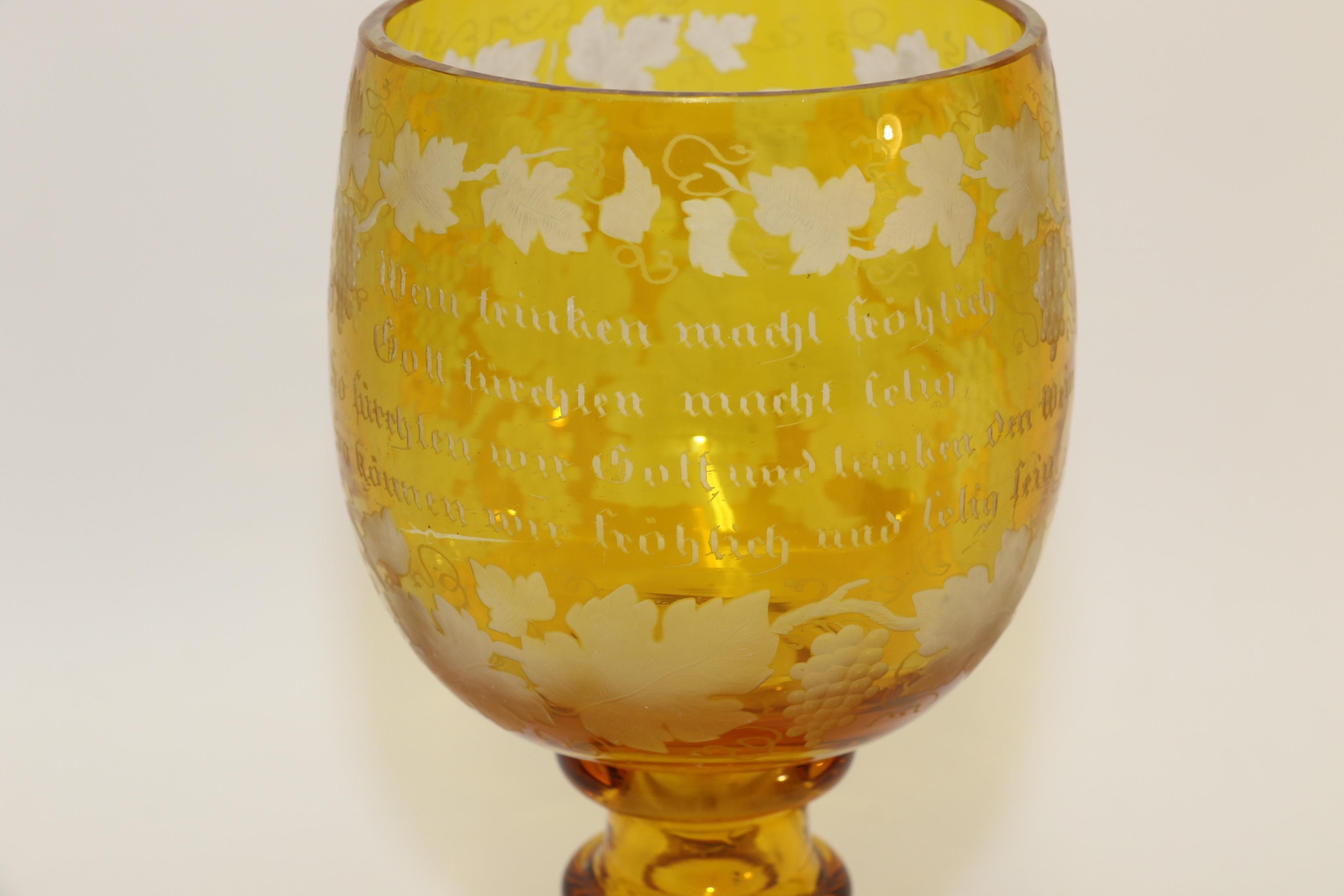This fine large German late 19th century amber glass goblet is made from clear glass which is overlaid in amber. The finely decorated bowl is skillfully cut and engraved through to the clear with an inscription on one side and a cherub drinking wine