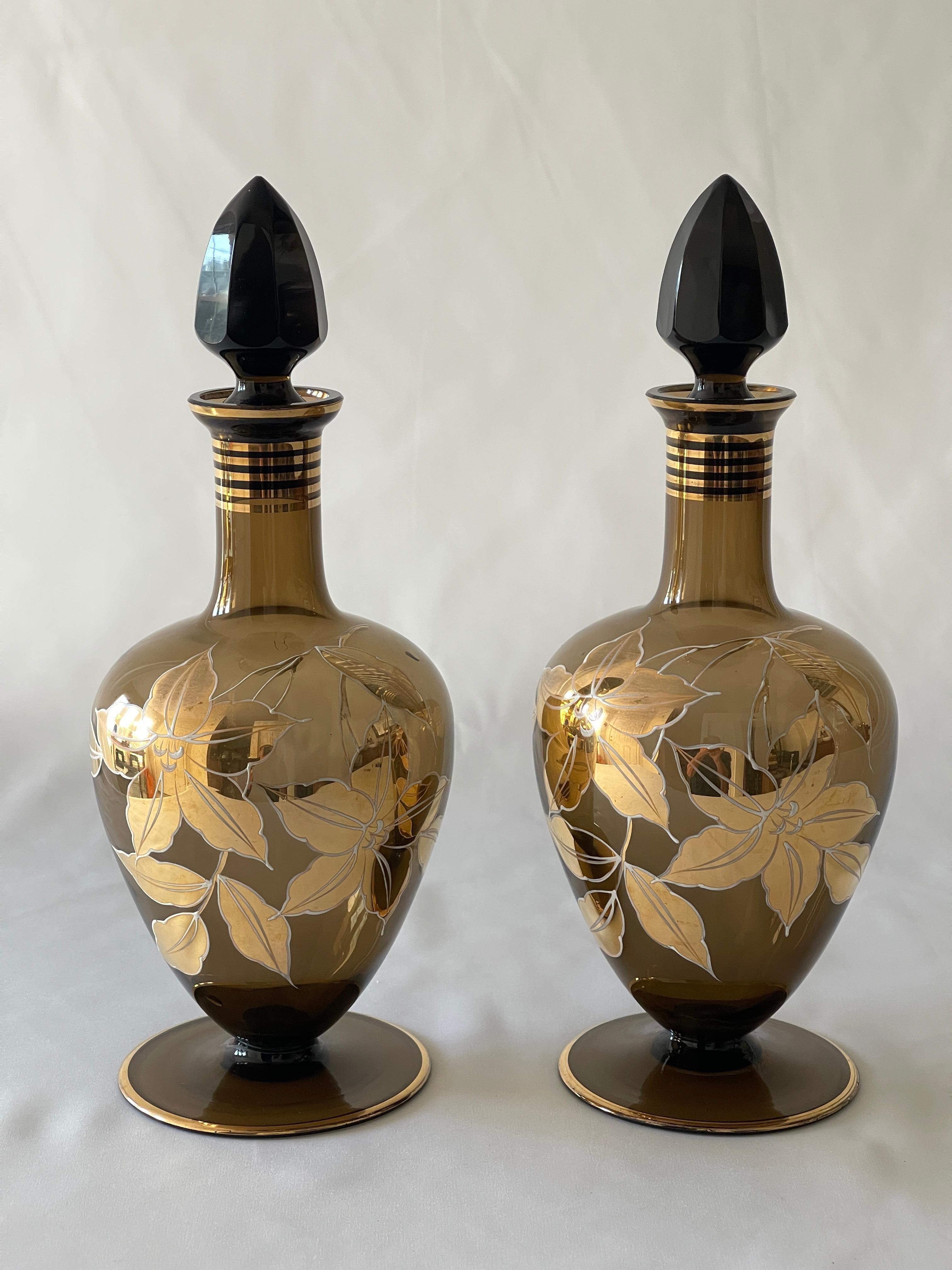 Lustrous German Mid Century smoke glass decanter set , finely hand decorated with 22K gold and enamel. Set includes two decanters with faceted dark smoke glass stoppers and a covered glass dish. 
The set is in excellent condition.
