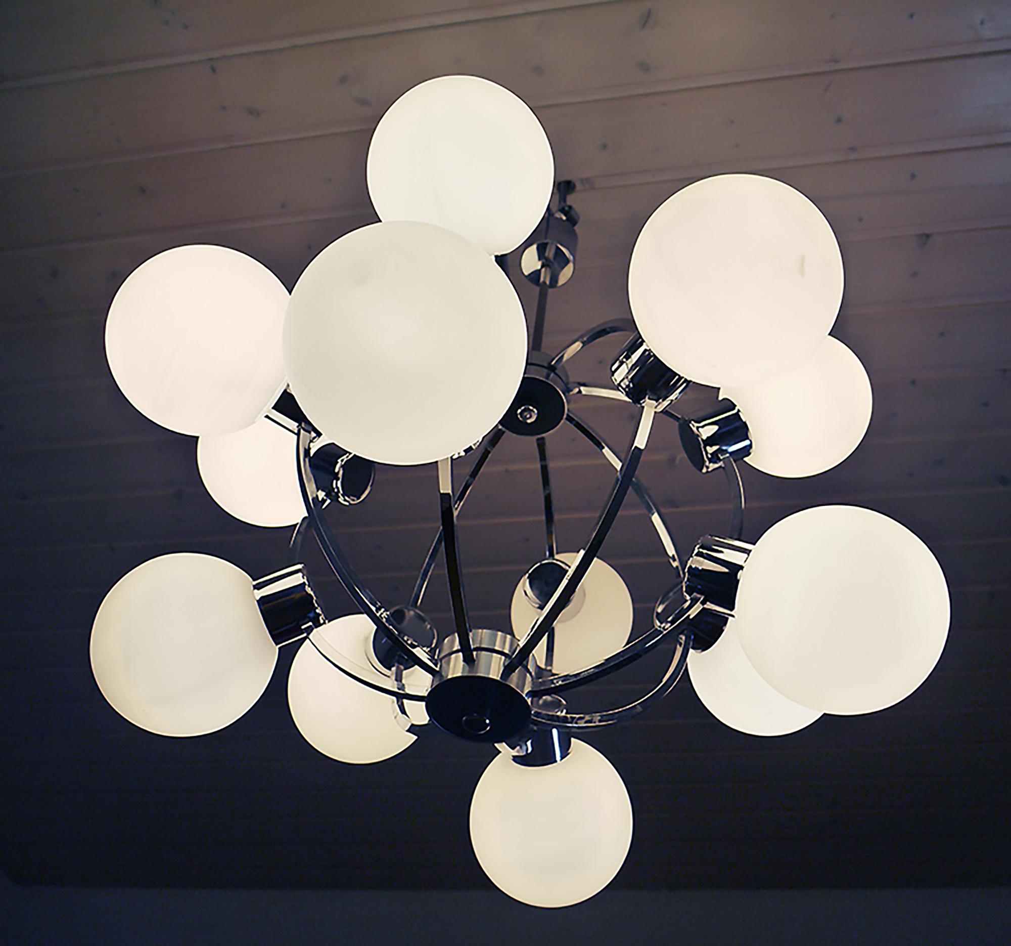 Elegante lampadario Sputnik a struttura atomica con dodici sfere di vetro bianco su una struttura in metallo cromato. Il lampadario si illumina magnificamente e offre una grande quantità di luce. Prodotto da Kaiser, Germania, negli anni '70. 
