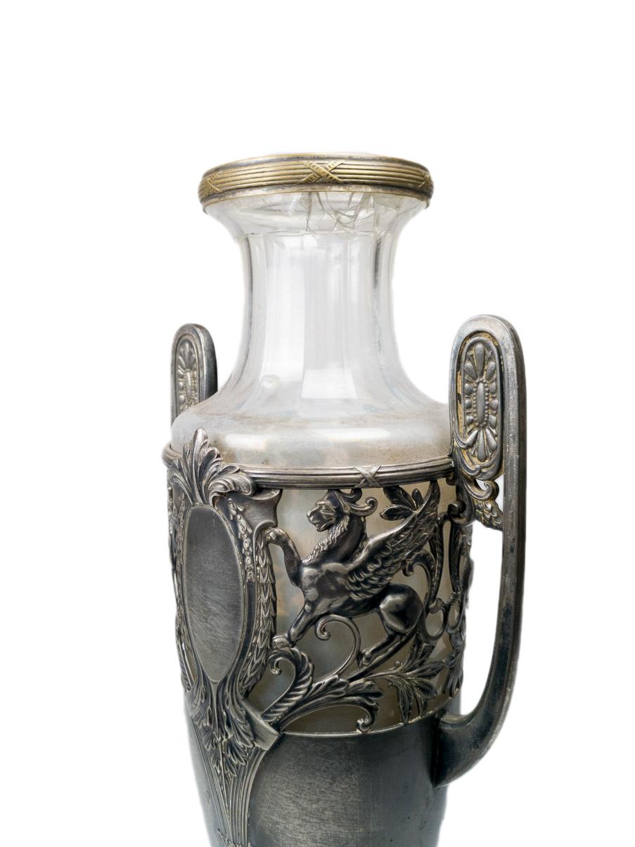Amphora-Vase aus versilbertem Zinn und Glas mit griechischen Figuren über die gesamte runde Länge des Wulstes, zwei Greifen, die den Gott Apollo darstellen (Greif halb Adler halb Löwe).
Leicht gesprungenes Glas am Hals.
Markierung 