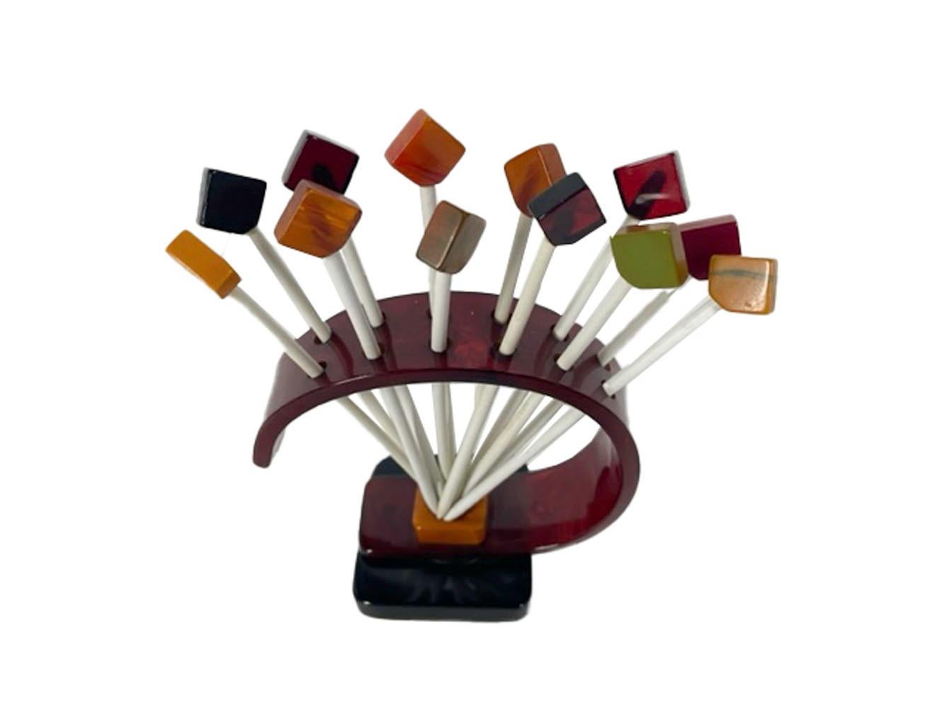 Set of 12 Art Deco cocktail picks in Bakelite stand. Picks with square tiles of various colors of Bakelite set diagonally on white wood picks stand in an arched support of tortoise, butterscotch and black Bakelite.