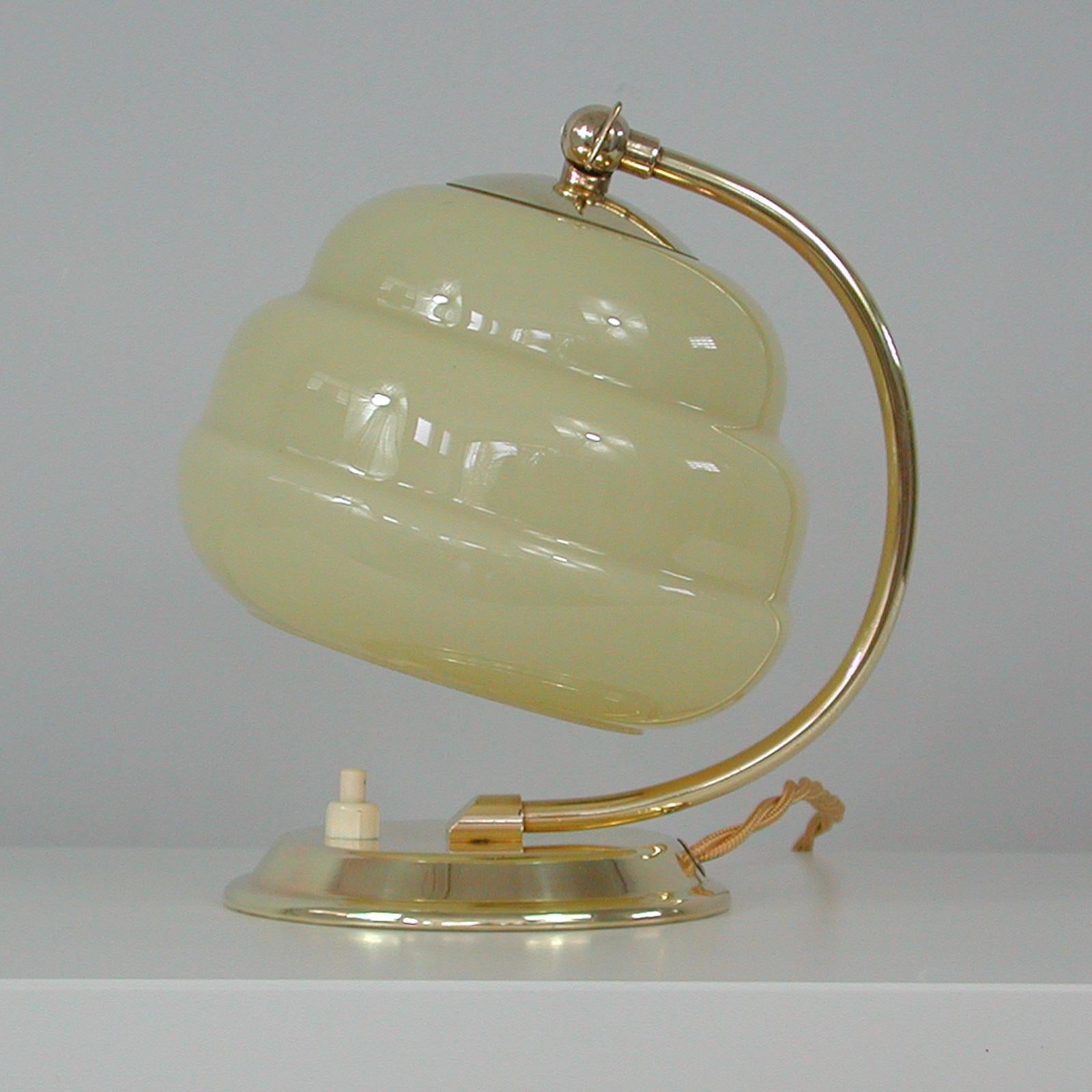 This unusual vintage table or bedside lamp was made in Germany in the 1930s-1940s during the Art Deco / Bauhaus period. It features a brass lamp base, brass lamp arm and an adjustable beehive shaped lampshade in ivory colored opaline glass. Original