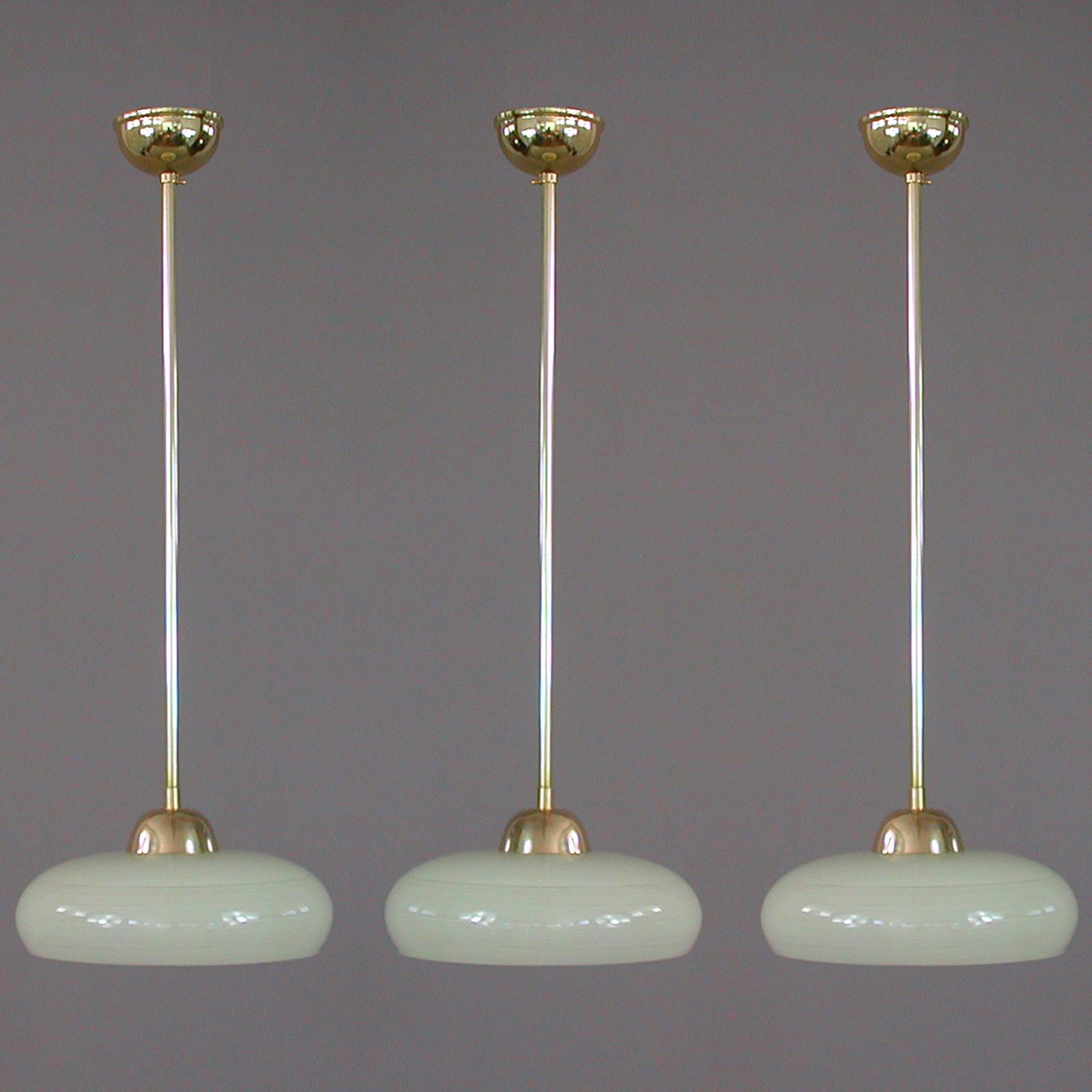 This elegant German pendant was designed and manufactured in Germany in the 1930s. The light features a cream colored opaline glass shade in typical Bauhaus design with striped glass decor and brass hardware. Good vintage condition with one E27