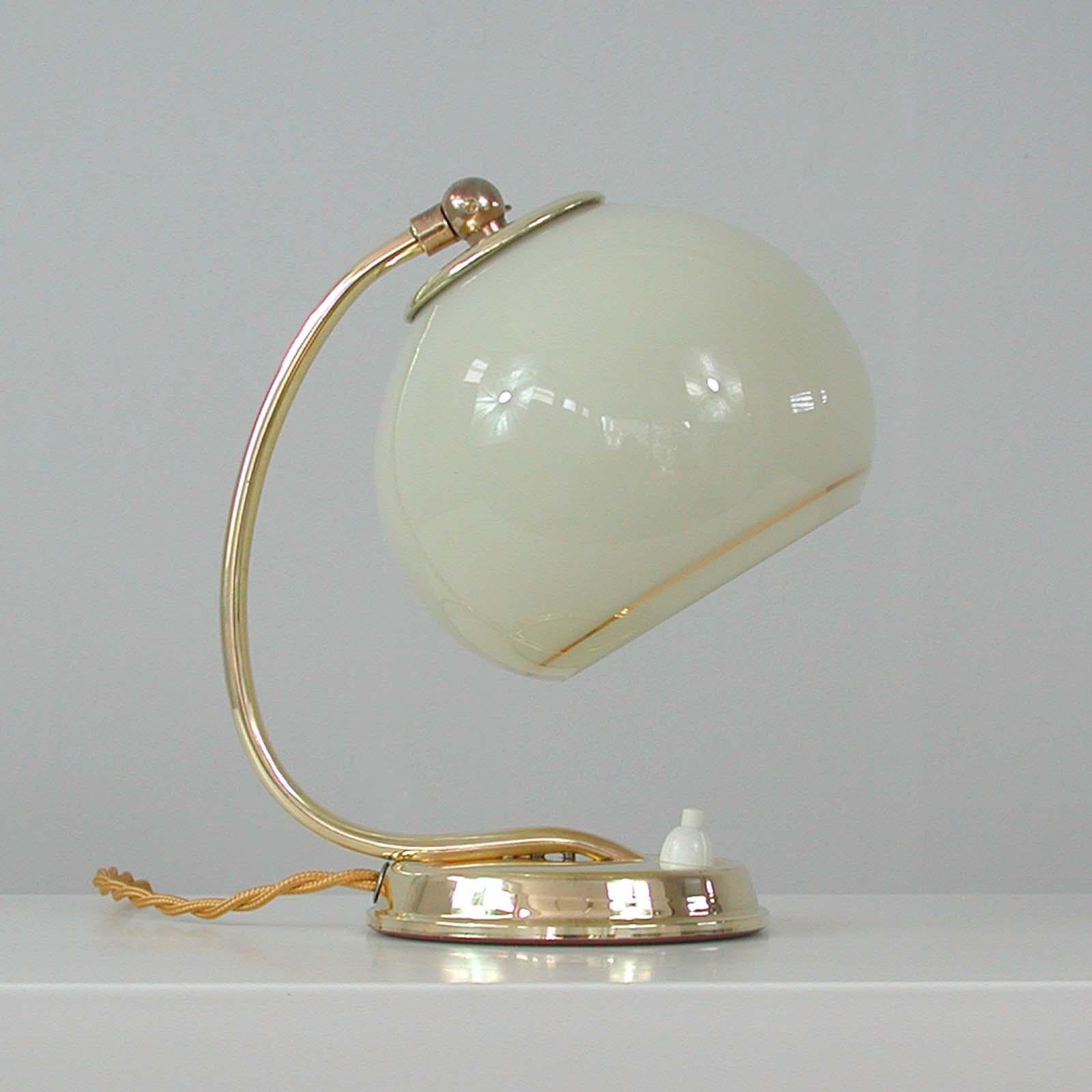 This awesome vintage table or bedside lamp was made in Germany in the 1930s during the Art Deco period. It is made of brass and has got an adjustable lamp shade in cream opaline glass with gilt decoration.

Rewired with gilt colored silk cord and