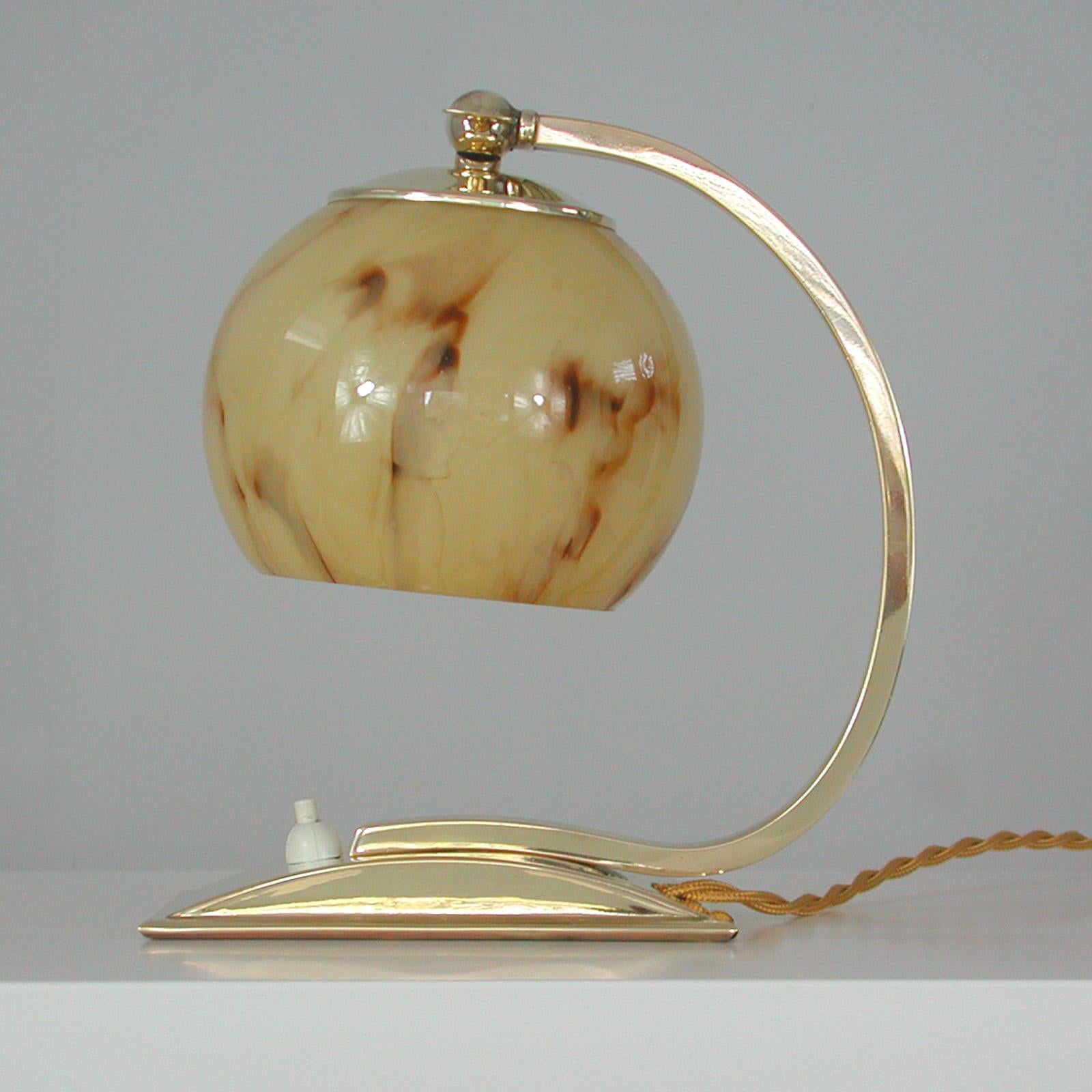 Cette lampe de table ou de chevet vintage inhabituelle a été fabriquée en Allemagne dans les années 1930-1940 pendant la période du Bauhaus. Il est fabriqué en laiton poli et possède un abat-jour réglable en verre opalin marbré crème.

La lampe