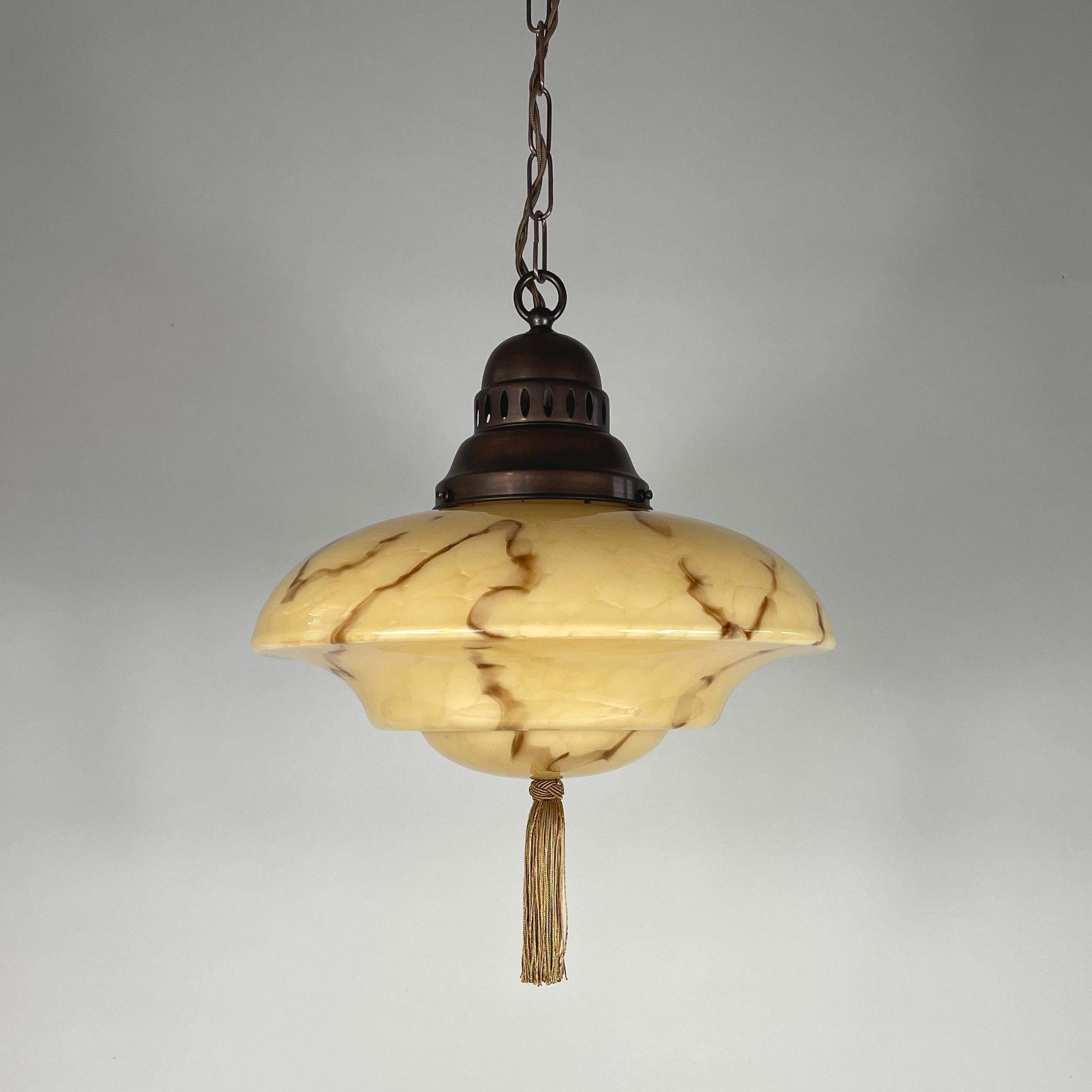 This unusual Art Deco fixture was designed and manufactured in Germany in the 1920s to 1930s during the Bauhaus period. It features a dark cream colored marbled glass lampshade, a bronze silk tassel and bronzed brass hardware.

The light has been
