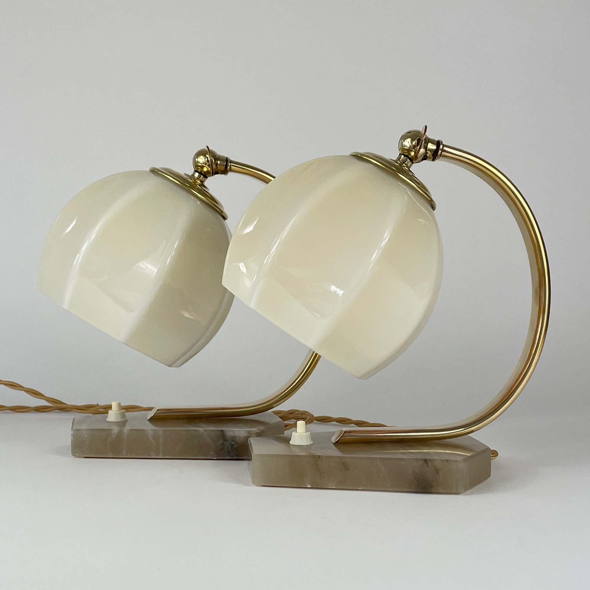 These unusual table or bedside lamps were designed and manufactured in Germany in the 1930s during the Art Deco / Bauhaus period. They feature dark cream colored alabaster bases, brass lamp arms and cream colored opaline lampshades. The lamps shades