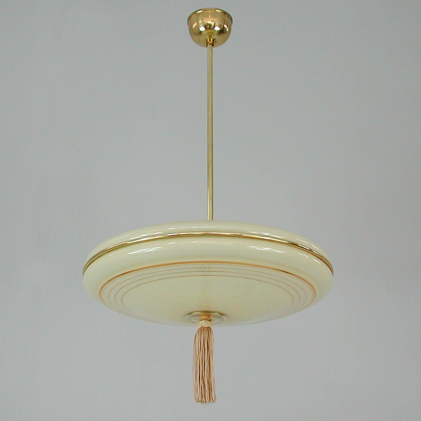 This elegant German pendant was designed and manufactured in Germany in the 1930s. The light features an ivory colored opaline glass lamp shade with gilt overlay decoration and brass hardware. This is a very typical Bauhaus Design. Very good vintage