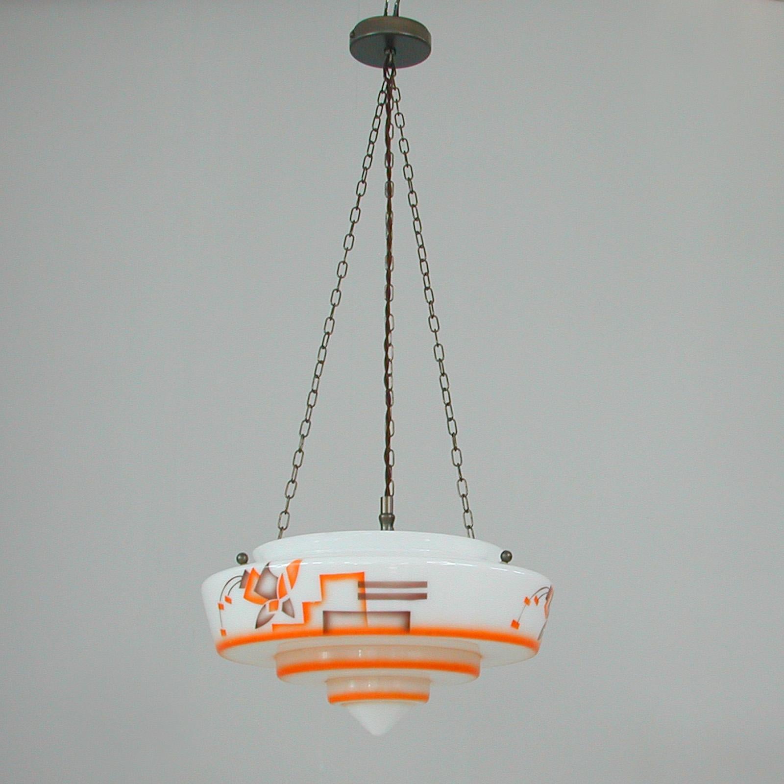 This unique Bauhaus inspired glass pendant was designed and manufactured in Germany in the 1930s. The light features a large tiered glass diffuser with enameled paintbrush decor in orange and brown. Suspended by patinated brass hardware. 

Good