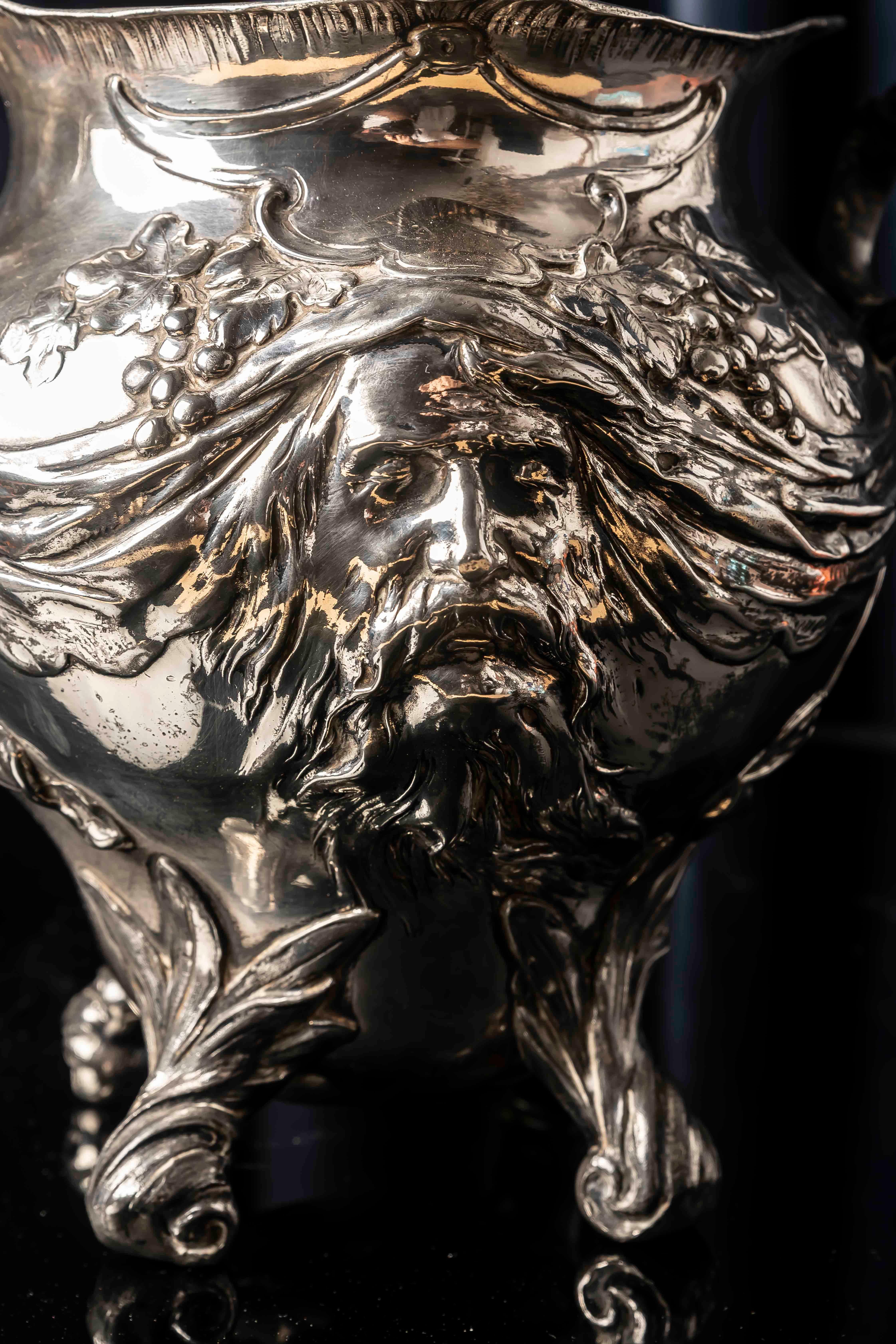 Ein ausdrucksstarker deutscher Jugendstil-Sektkühler von WMF, um 1900, mit einer mächtigen Bacchus-Maske im Hochrelief, umrahmt von Ranken, Weintrauben und fließenden Draperien. Die dichte Repoussé-Modellierung, das skulpturale Gesicht und die