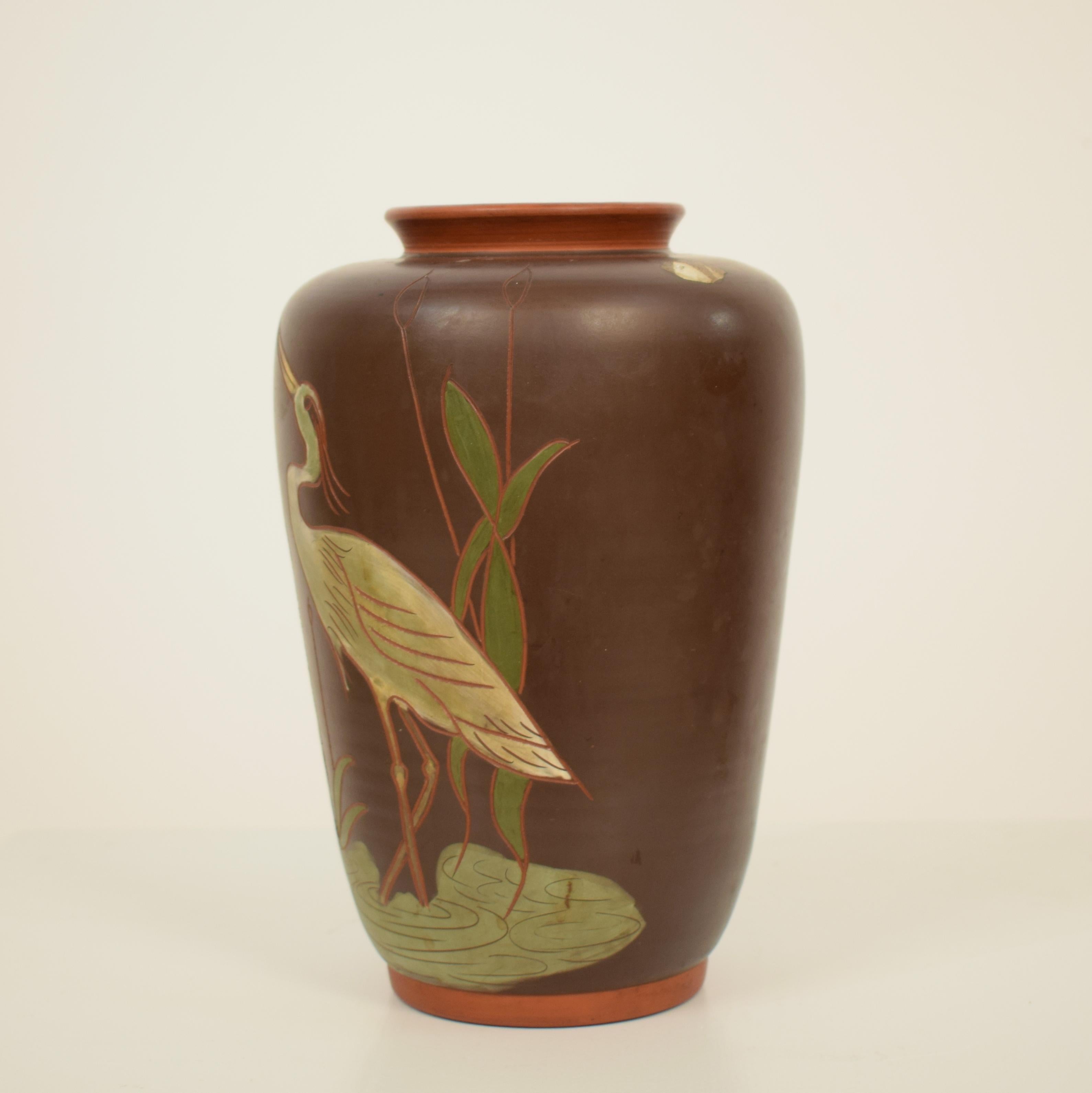 Diese schöne deutsche Jugendstil-Keramikvase wurde um 1910 hergestellt.
Sie hat einen braun bemalten Sockel und ist mit einem Kranich und Schilfrohr verziert. Typische Motive für diese Zeit.
Auf der Oberseite der Vase befinden sich Reste eines