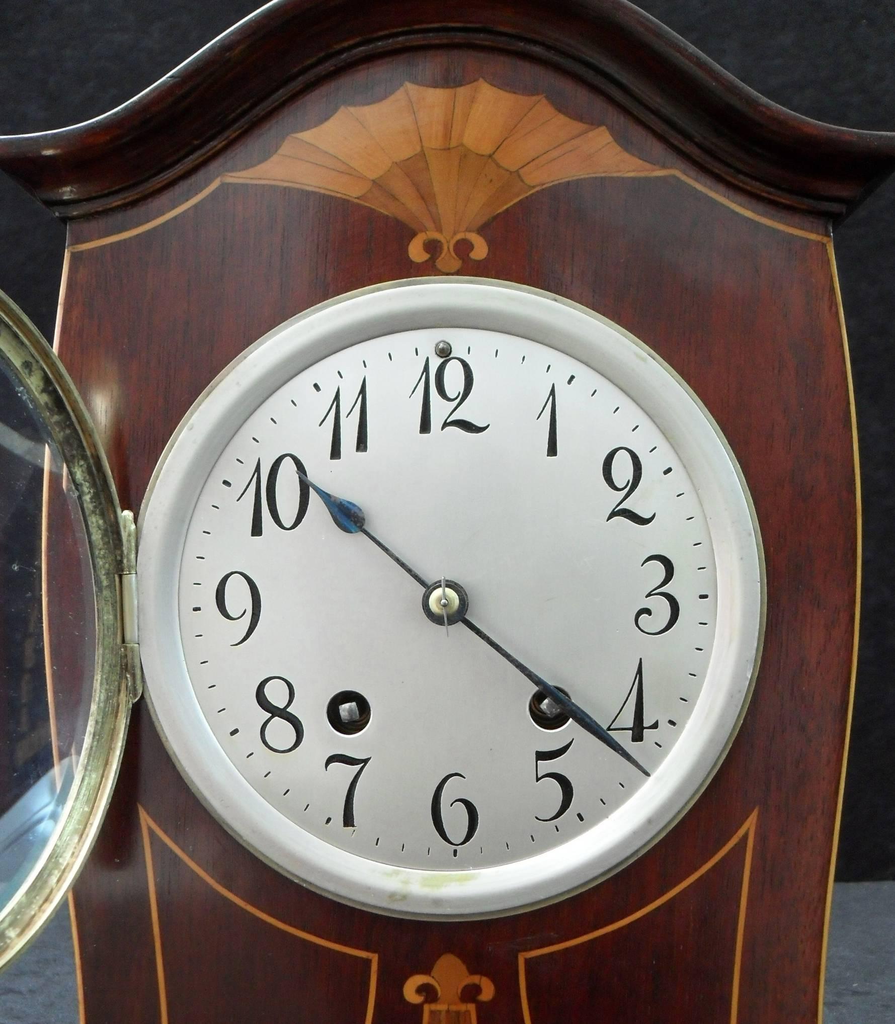 A decorative German Art Nouveau mahogany mantel clock with satinwood fan and boxwood string inlay to the front of the case, the clock has a silvered 5 inch dial with a German eight day Lenzkirch movement which strikes the hours and half hours on a