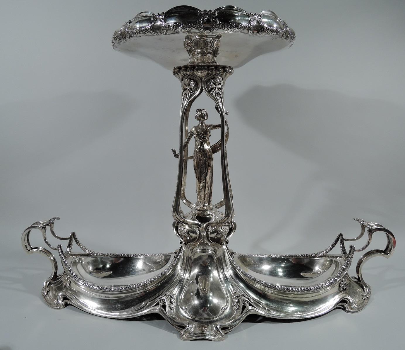 German Art Nouveau 800 silver centerpiece. Made by M. H. Wilkens & Söhne in Germany, circa 1900. Shaped base with ovoid wells. Flying anthropomorphic end handles with pendant garlands. Central open pergola with figure of bare-breasted Classical
