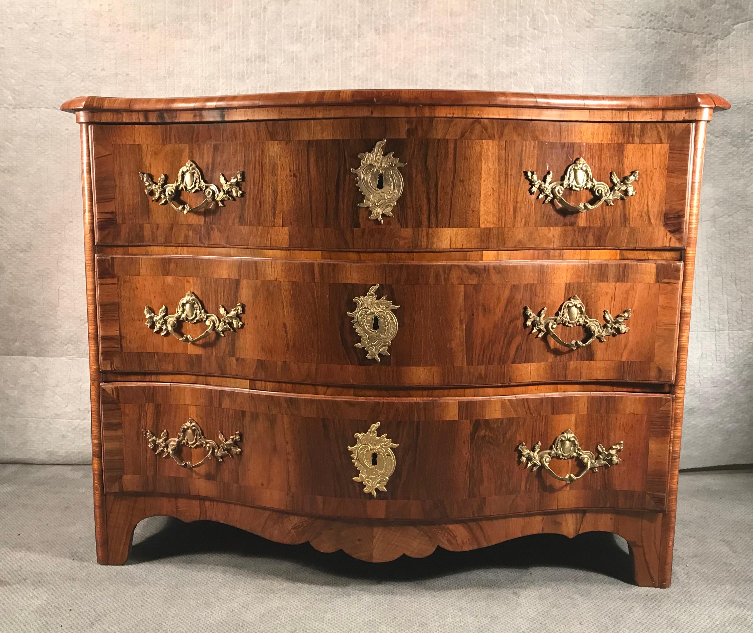 This beautiful German Baroque dresser dates back to circa 1750. It was probably made in the region of the city of Dresden.
Different walnut veneer grains embellish this original commode. The three drawers are decorated with the original bronze