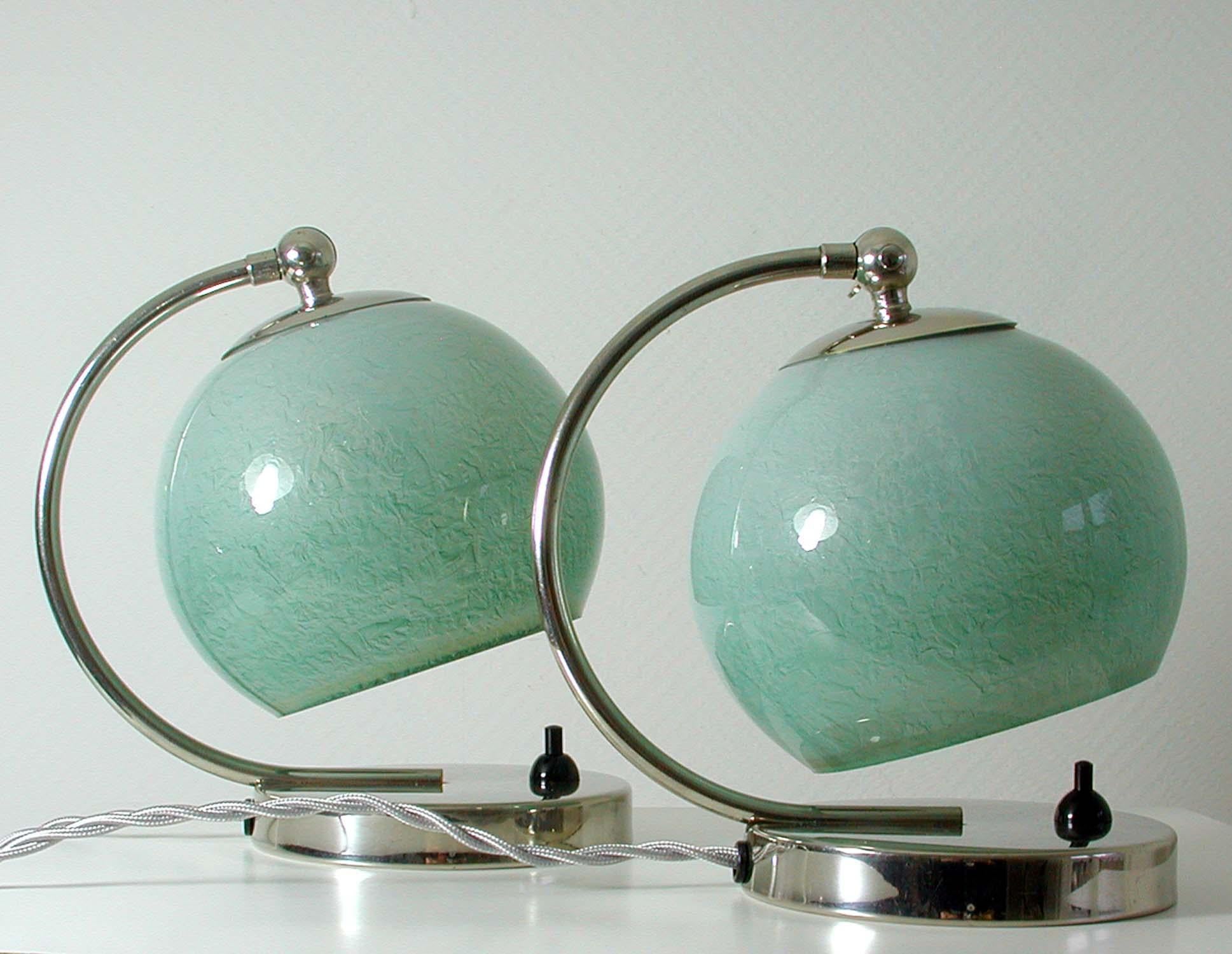 These table or bedside lamps were designed and manufactured in Germany in the 1930s during the Bauhaus period. They are made of chrome and have got mint colored / light greenish-blue opal glass lamp shades.
They can be used as table lights as well