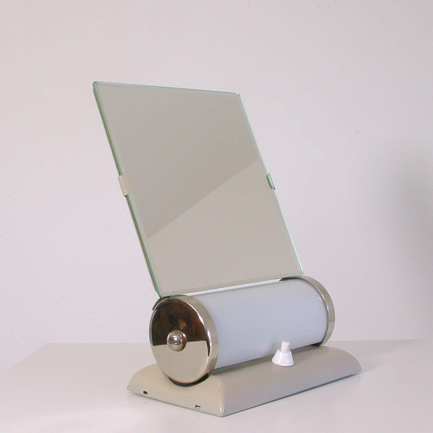 This Bauhaus inspired table mirror was designed and manufactured in Germany in the 1930s-1940s in the manner of Ruppelwerke, Gotha.

It has got a cream lacquered base, an adjustable bevelled mirror and an opaline lamp shade. All other parts are
