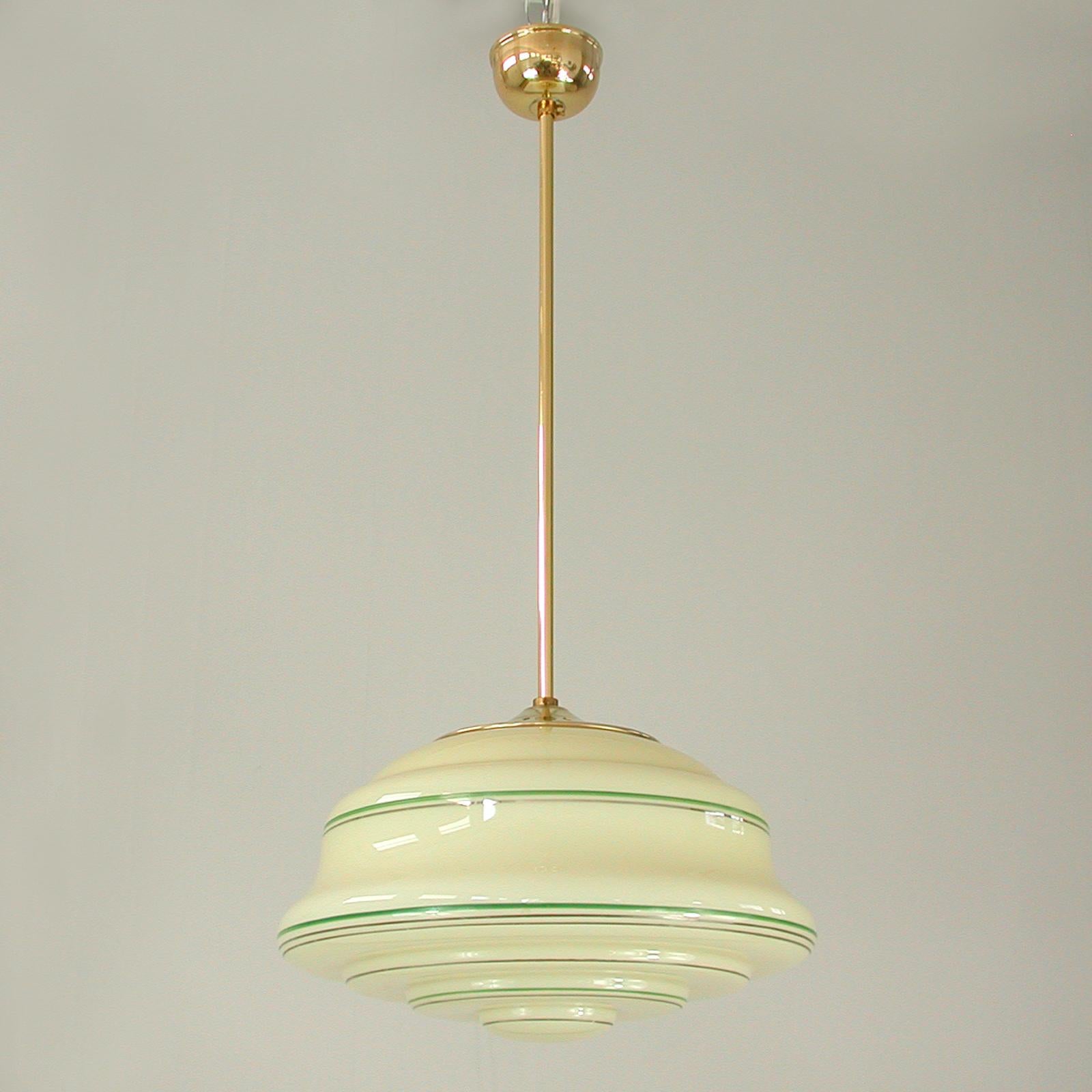 This beautiful Art Deco pendant was designed and manufactured in Germany in the 1920s-1930s. It features a cream colored Opaline lamp shade with brass details. The lamp shade has got a green and silver enameled decor. The light is in very good