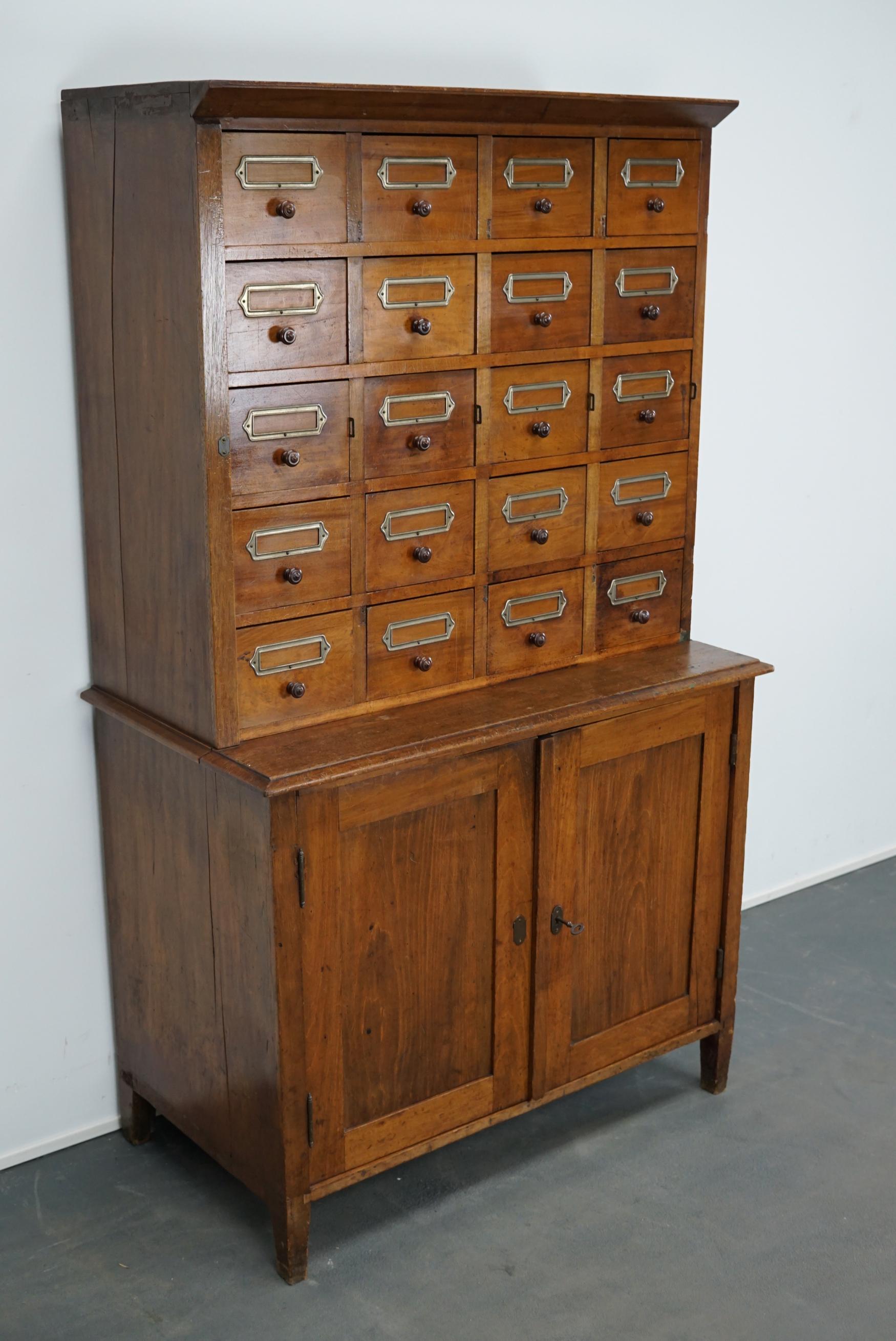 This apothecary cabinet was produced during the 1930s in Germany. This piece features 20 drawers with nice cardholders and wooden pulls. The interior dimensions of the drawers are: D x W x H 30 x 16.5 x 6.5 / 12 cm for the top drawers. The cabinet