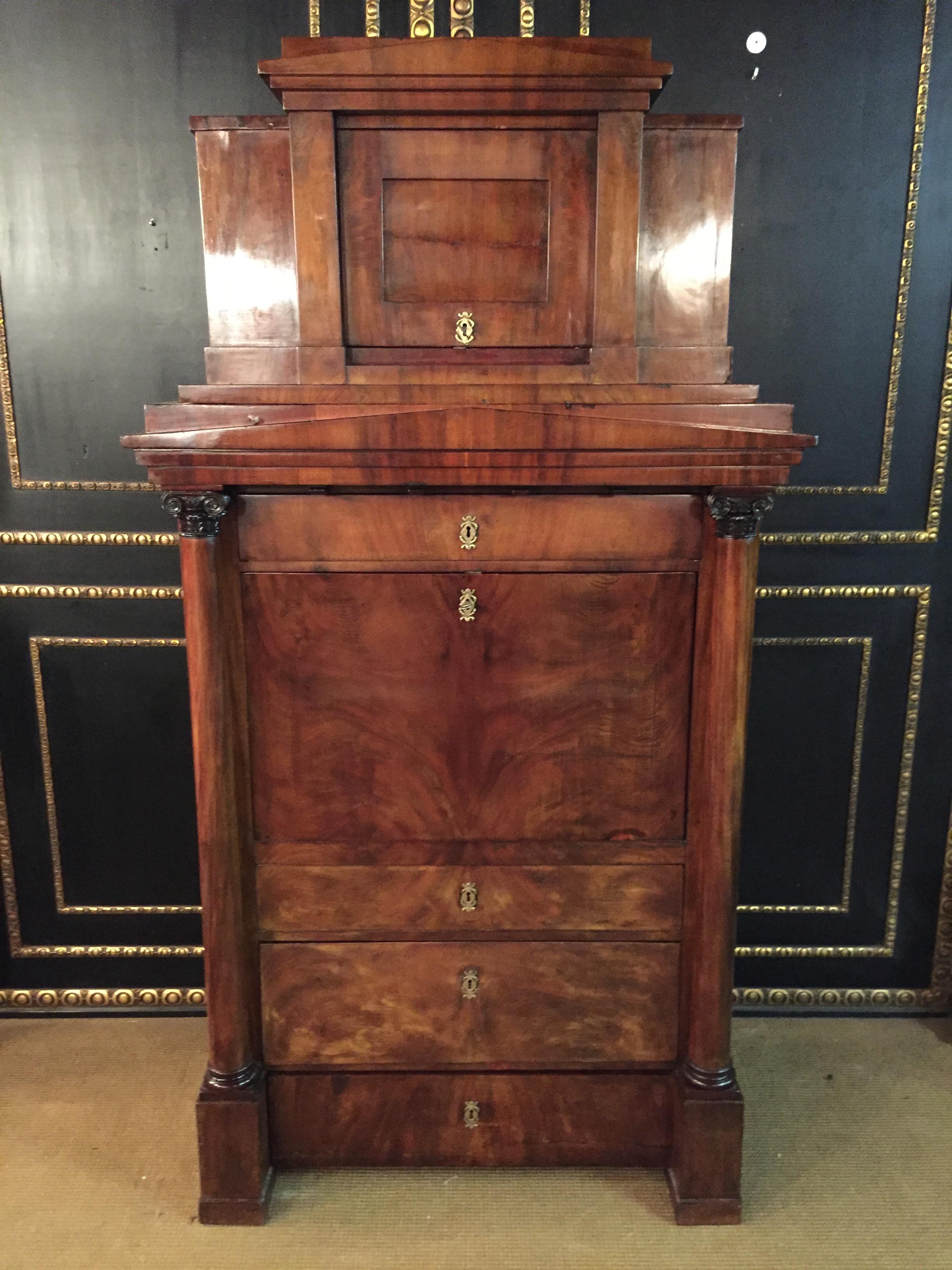 Early 19th century Biedermeier secretary cabinet composed of mahogany and featuring a series of drawers and on the top is a door as well as carved Corinthian column decorations.
  