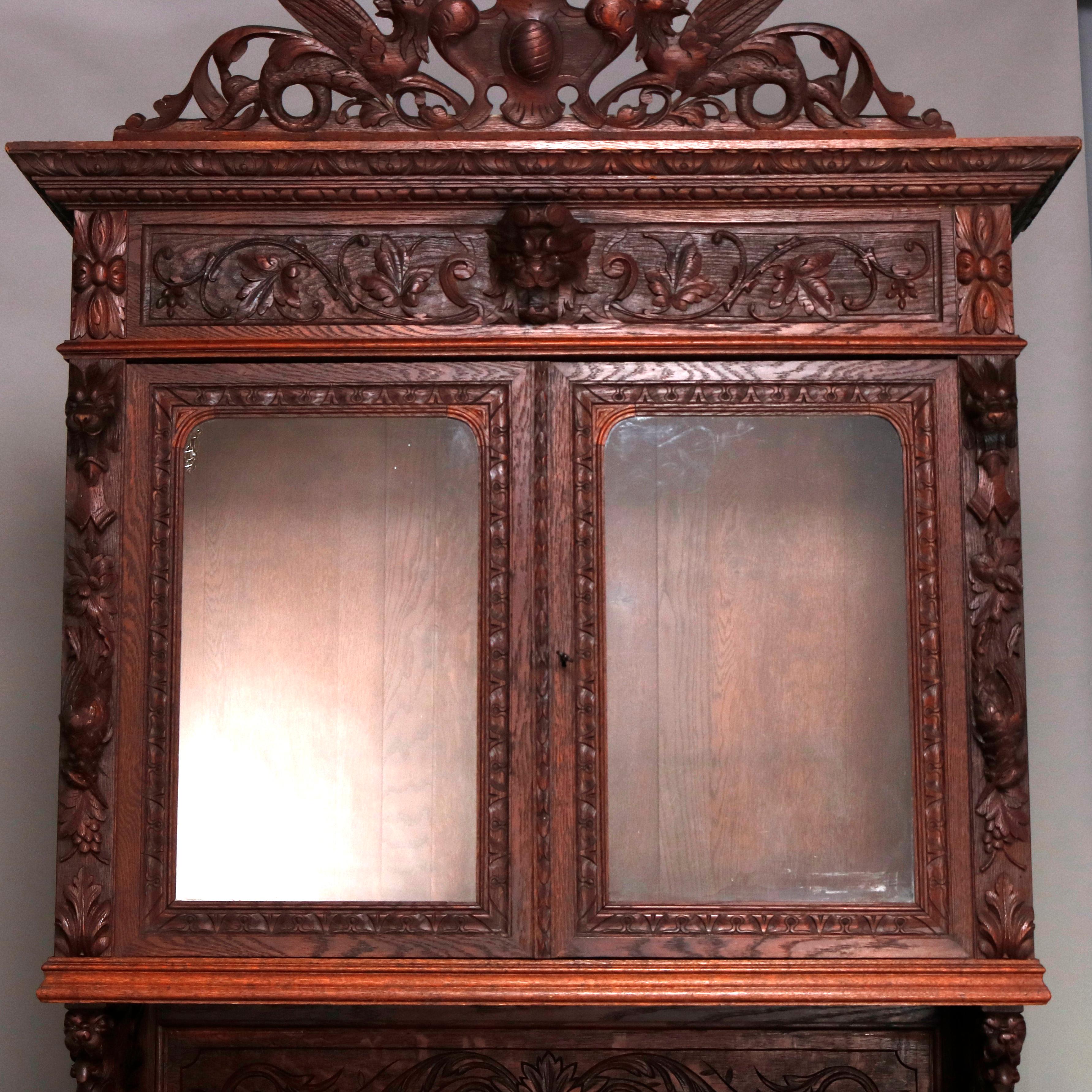 An antique German Black Forest figural hunt board breakfront cabinet offers oak construction with carved crest having central urn with flanking griffins and foliate decoration surmounting upper cabinet with double glass doors with carved griffin