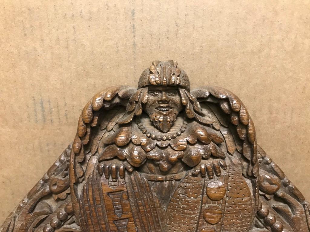 Very cool hand carved crest showing a helmeted Viking warrior figure with wings, holding two shields that also serve as coats of arms. Below him a 'Green Man' face with a bemused look and paws underneath. On either side of the shields are rondels