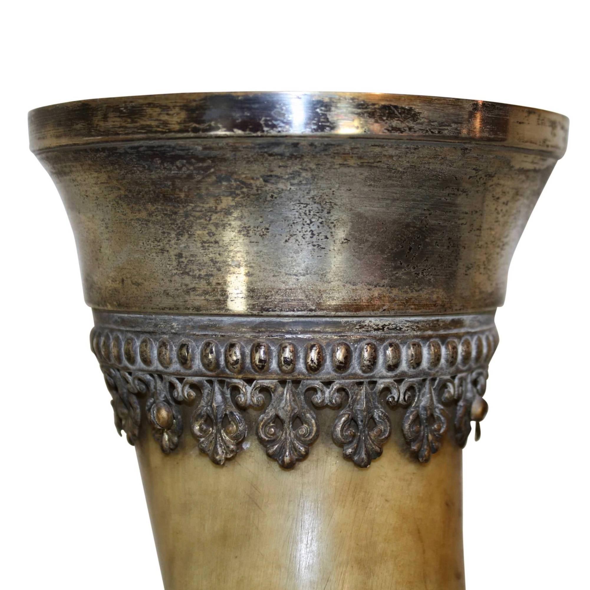 Handsomely adorned with a silver plated rim and supported by a brass stand, this German drinking horn is in very good condition. A single stag stands on the round base, overshadowed by an oak tree. The trunk of the tree supports a decorative collar