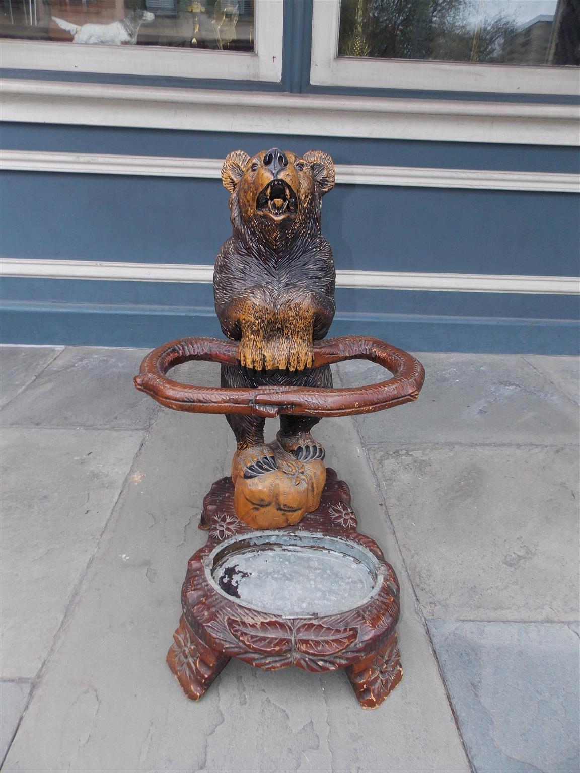 German carved and painted walnut Black Forrest umbrella / cane stand with a standing bear on a river rock, open mouth, glass eyes, paws supporting a stylized loop snake branch, inset tin drip pan, and resting on a rocky plinth with four carved