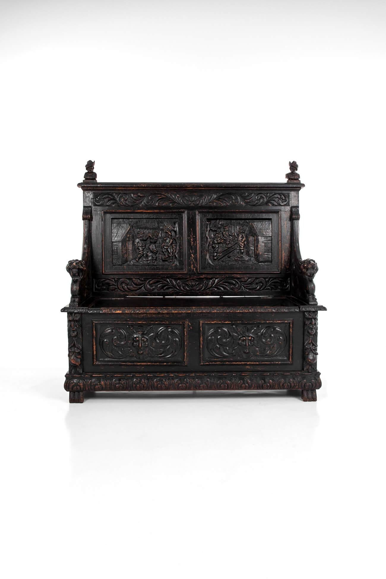 A superb German carved oak settle. Featuring two bust finials on its straight crest rail and a high seat back intricately carved with scroll motif and floral leaf surrounding two carved scenic panels. The seat, which is flanked by curved armrests