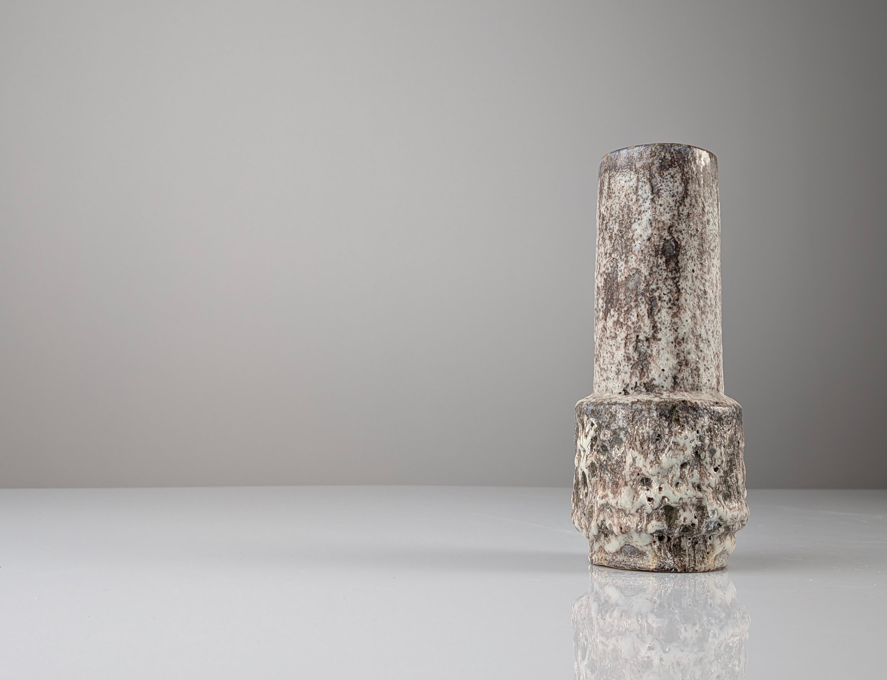 Questo vaso in ceramica tedesca, rappresentativo dello stile Fat Lava, è un eccezionale esempio di design moderno della metà del secolo scorso. La sua texture ricca e vulcanica, caratteristica della tecnica Fat Lava, crea un affascinante contrasto