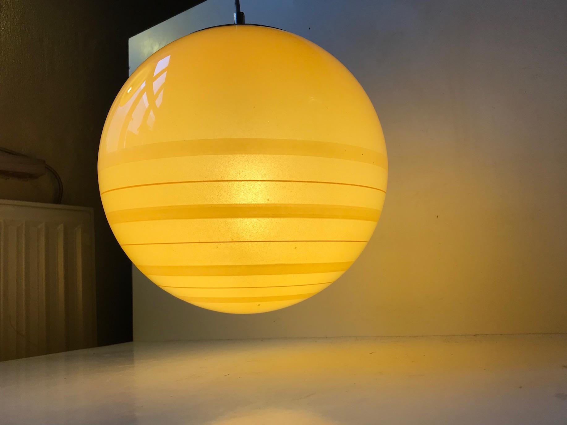 A rare spherical pendant light in yellow opaline glass the half of which is decorated with horizontal stribes. It has a nickel plated top that allows for easy access when the bulb need to be changed. It was manufactured by Peill & Putzler in Germany