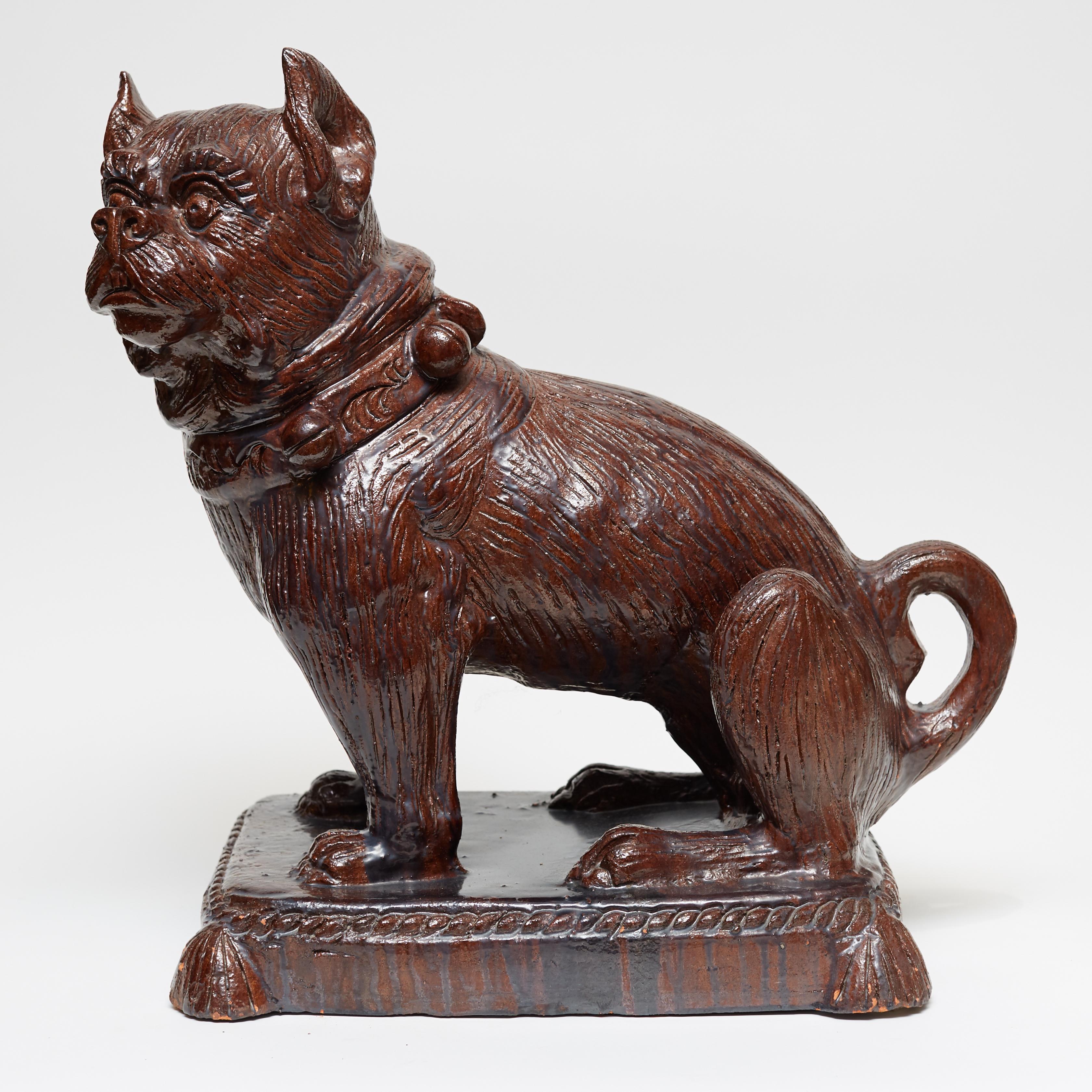 German figure of a seated bulldog on tasseled pillow carved from terracotta with a carmel brown glazed finish.