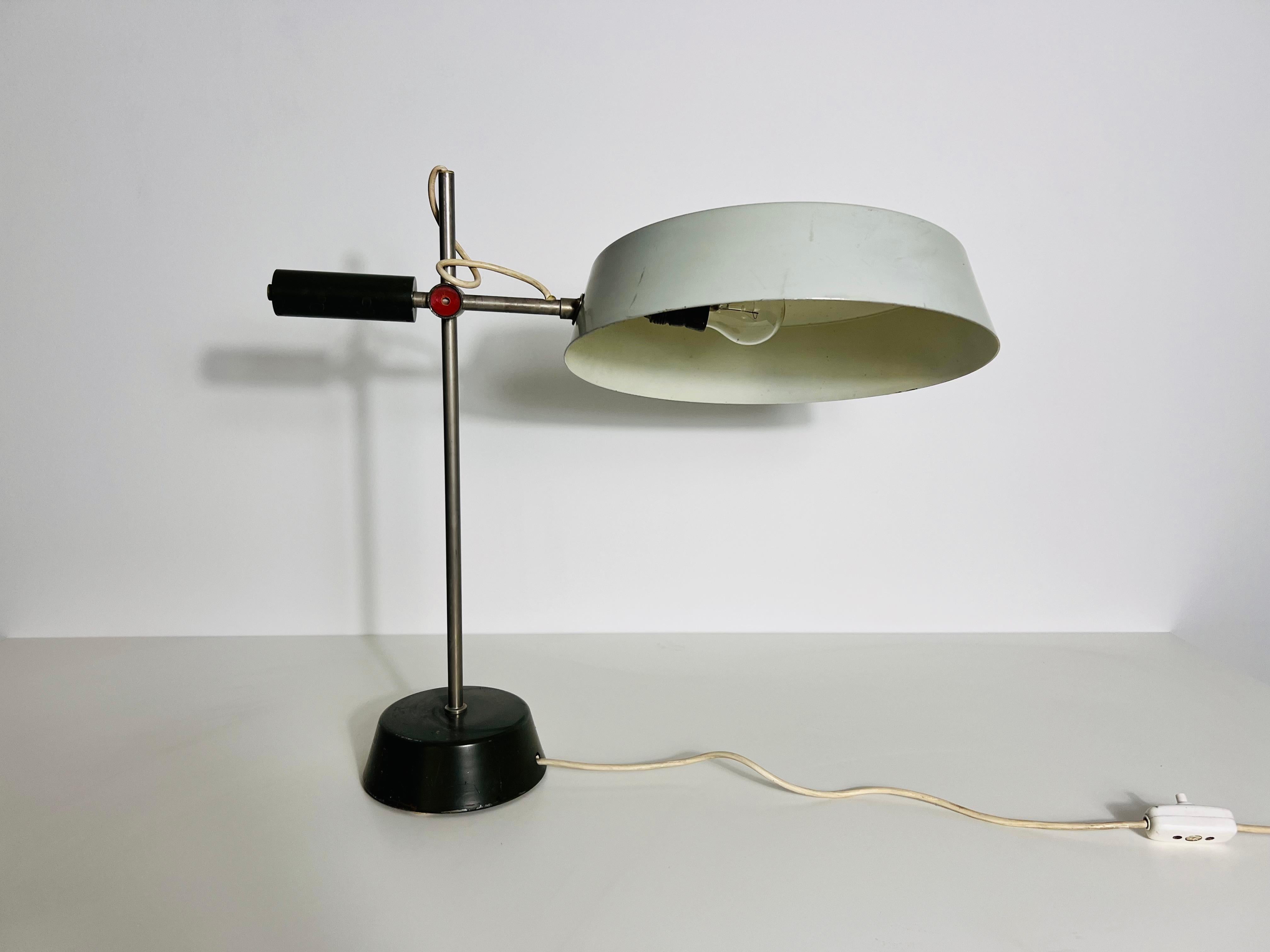 Esta lámpara de mesa vintage, fabricada en Alemania en la década de 1960, es un impresionante ejemplo de diseño inspirado en la Bauhaus. Con una elegante varilla de aluminio cromado y una robusta base de metal negro, esta lámpara combina