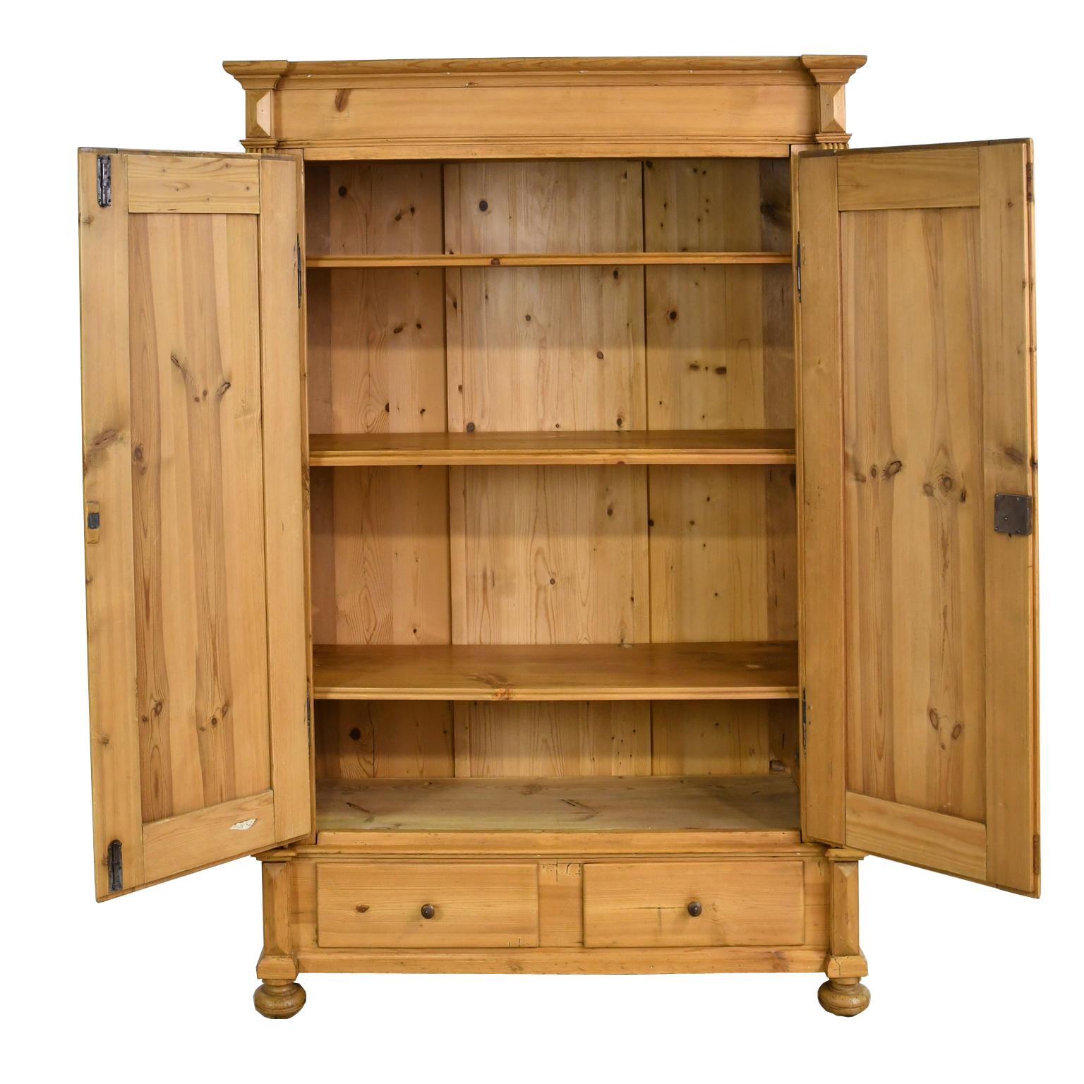 A German Gründerzeit armoire in scrubbed pine with two doors that have raised panels and open to three adjustable interior shelves, with two exterior storage drawers along the bottom. Offers all the original components including period hardware with