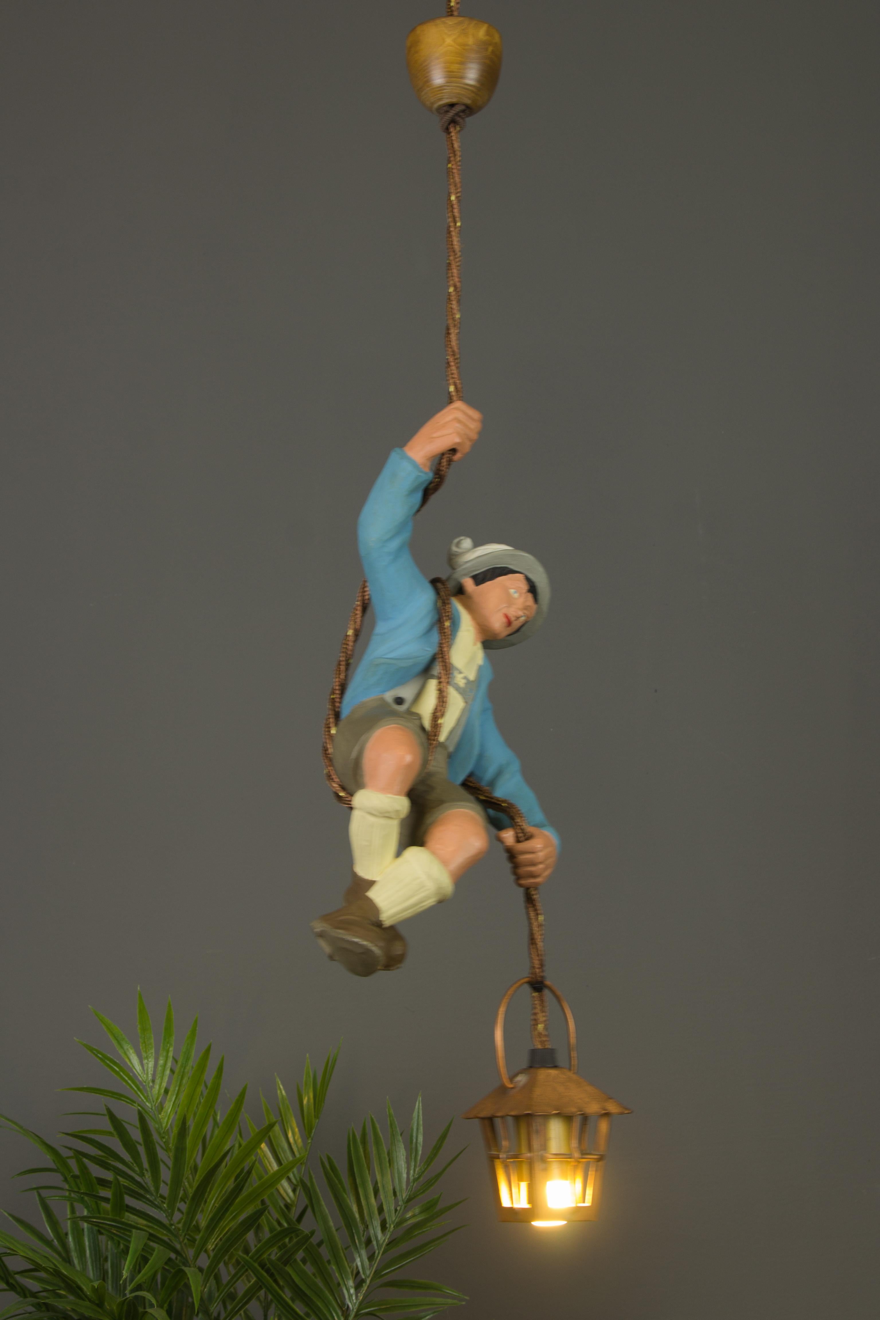 Wonderful German figural pendant lamp features a hand-carved and hand-painted figure of a Bavarian mountain climber. The detailed carved wooden man is holding onto a rope and holding a copper lantern in one hand. The figure has a blue-painted