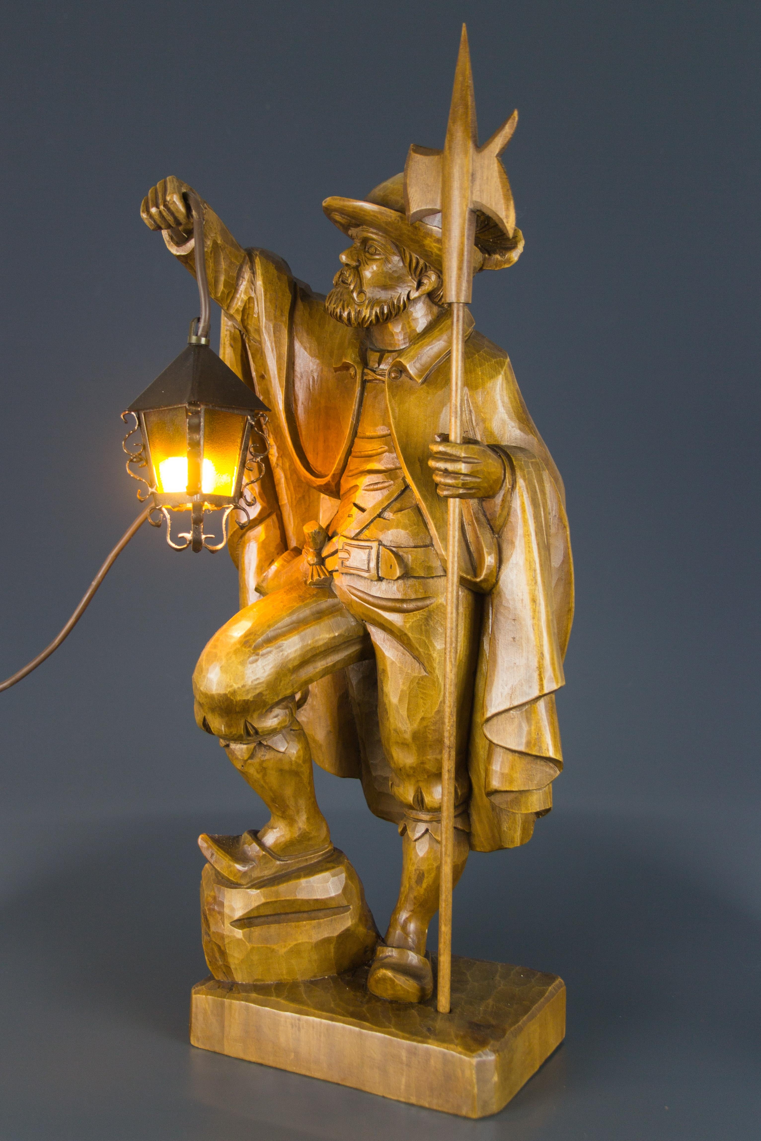 A masterfully hand carved wooden lamp features a large sculpture of a night watchman with a lantern and halberd. Lantern is made of glass and iron. This beautiful sculpture lamp can be used as a floor or a table lamp. Germany, mid-20th century.
One