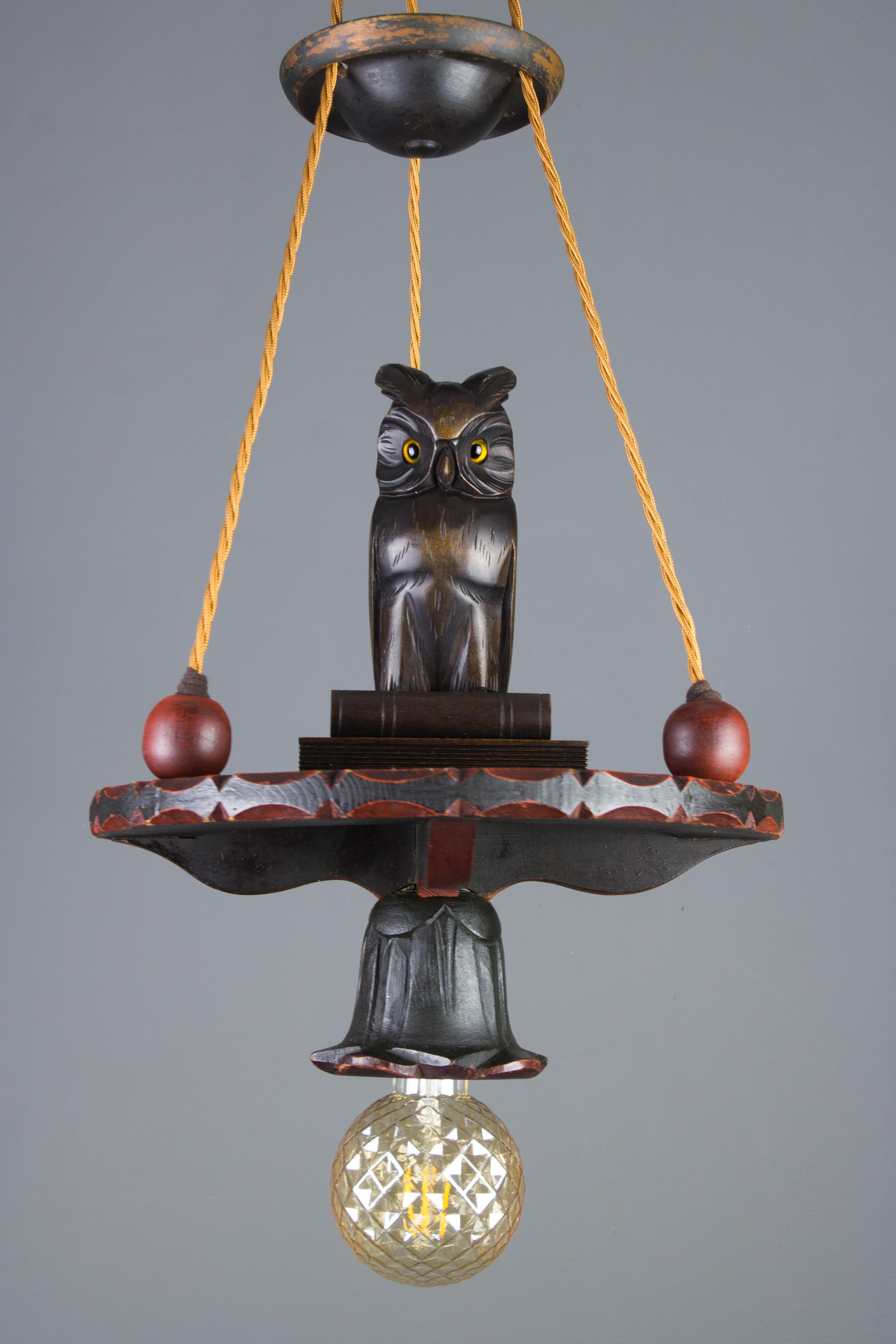 A beautiful hand-carved wooden pendant light, chandelier with an adorable, detailed carved sculpture of an owl, sitting on books in the center of the chandelier. In Greek mythology, a little owl (Athene noctua) traditionally represents or