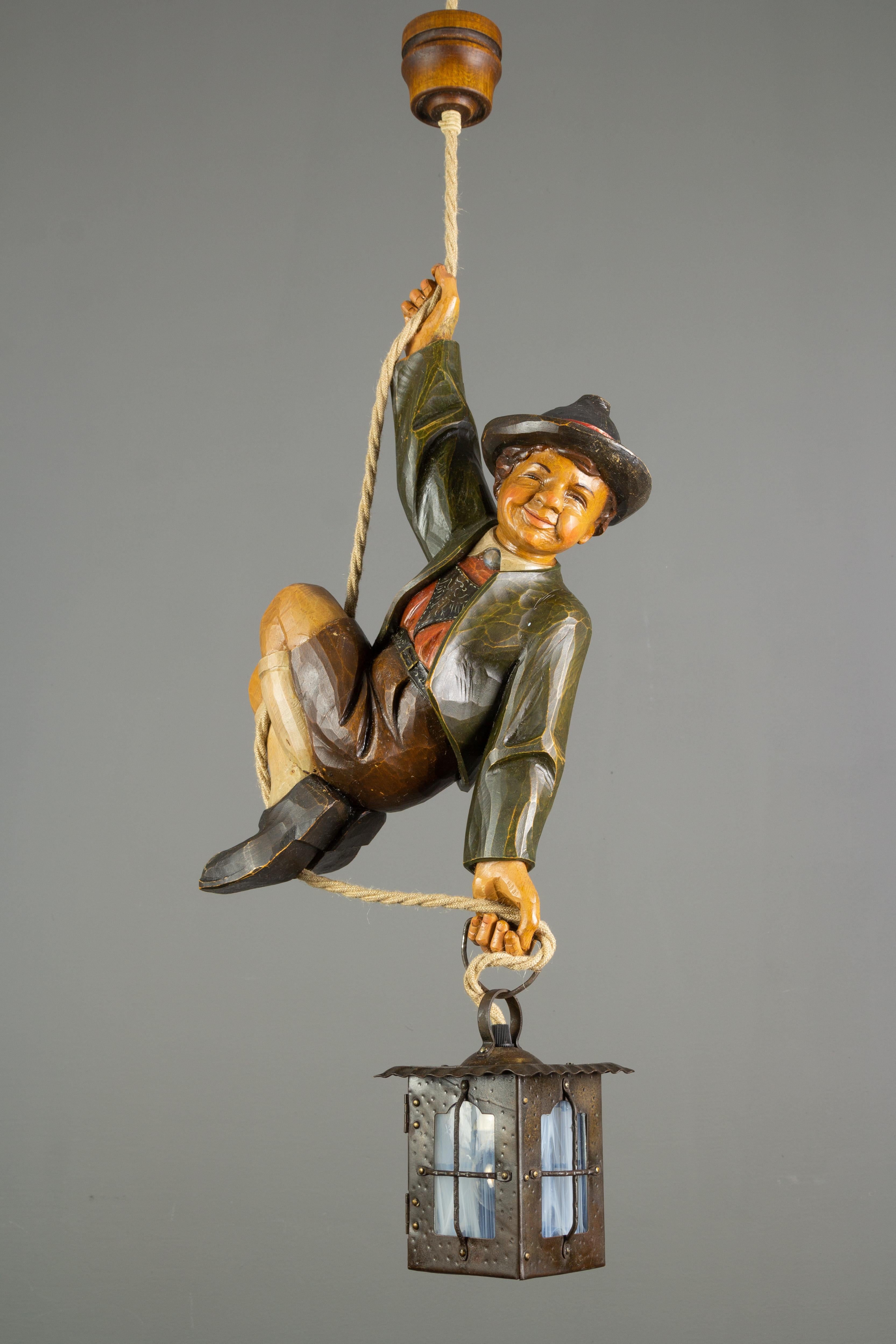 Wonderful German pendant lamp features a hand-carved figure of a smiling and cheerful mountain climber in beautifully hand-painted Bavarian traditional clothing in brown, green, white, and red colors. The detailed carved wooden figure wears a hat