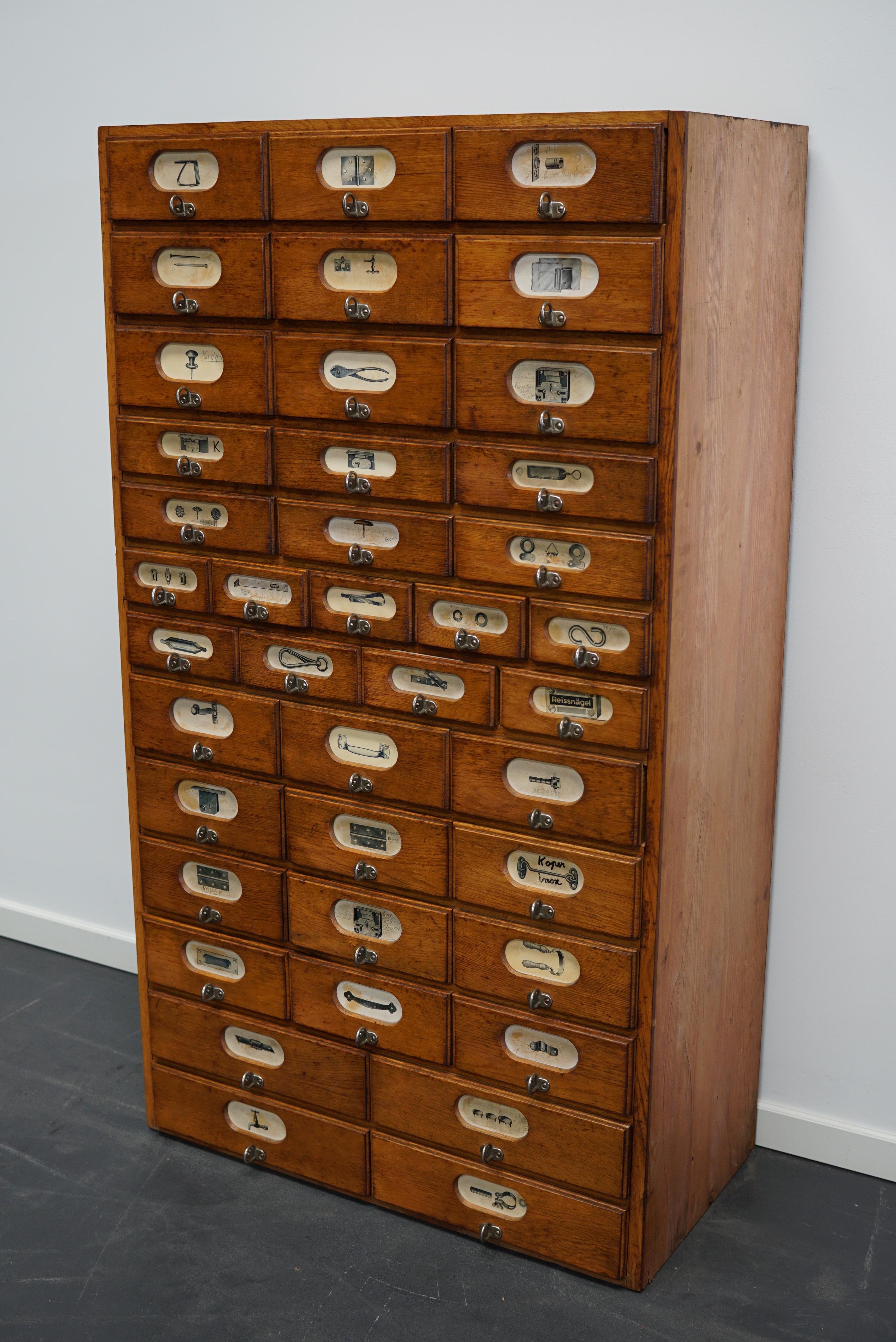 This apothecary cabinet was made circa 1940s in Germany and was later used in a hardware store in Belgium until recently. It features many drawers in different sizes with metal handles and the labels of the contents.